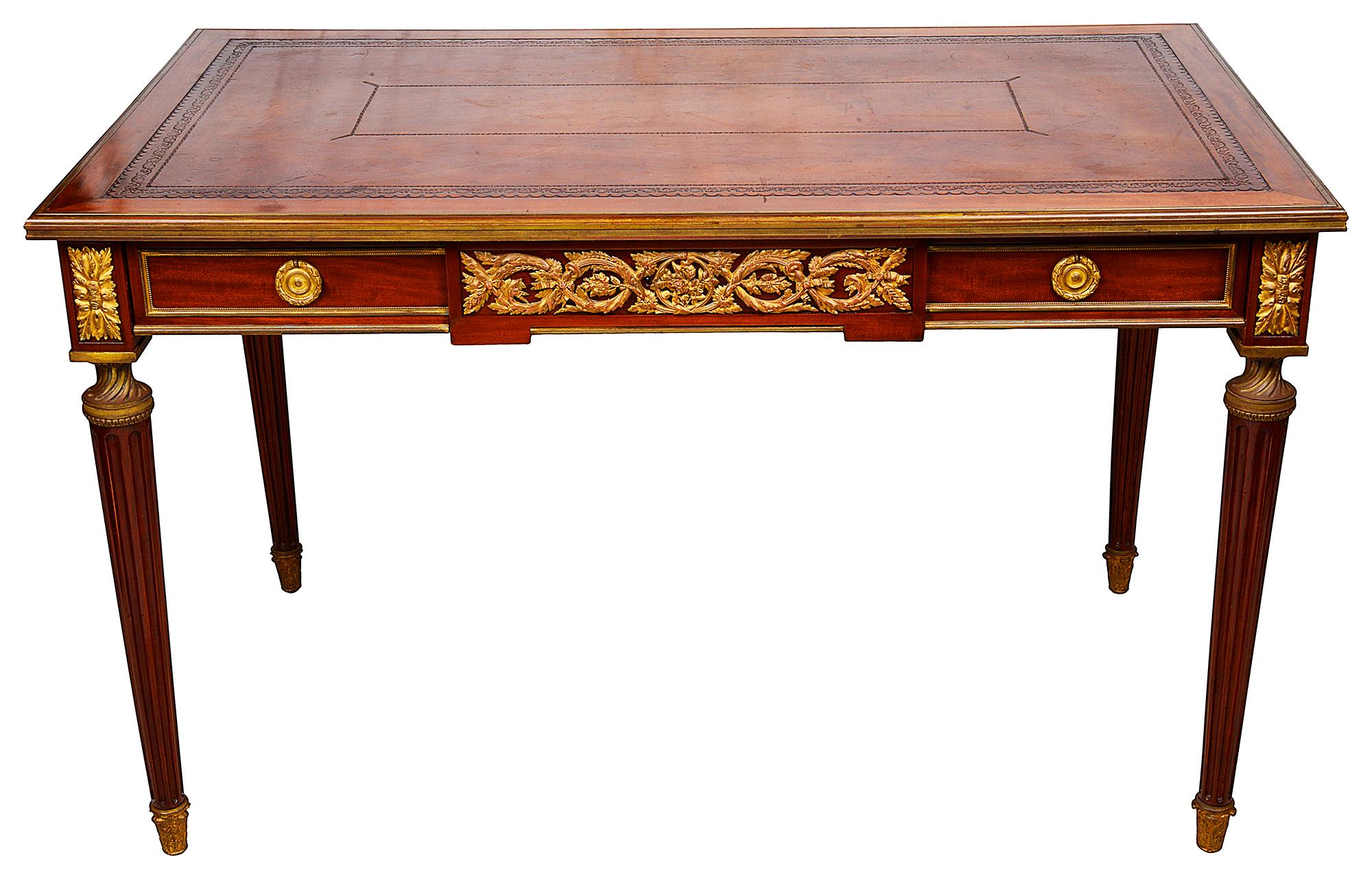 A very good quality 19th century French Louis XVI style mahogany bureau plat. Having an inset leather top, gilded ormolu mouldings and scrolling foliate mounts to the frieze, two frieze drawers and raised on turned tapering fluted legs, terminating