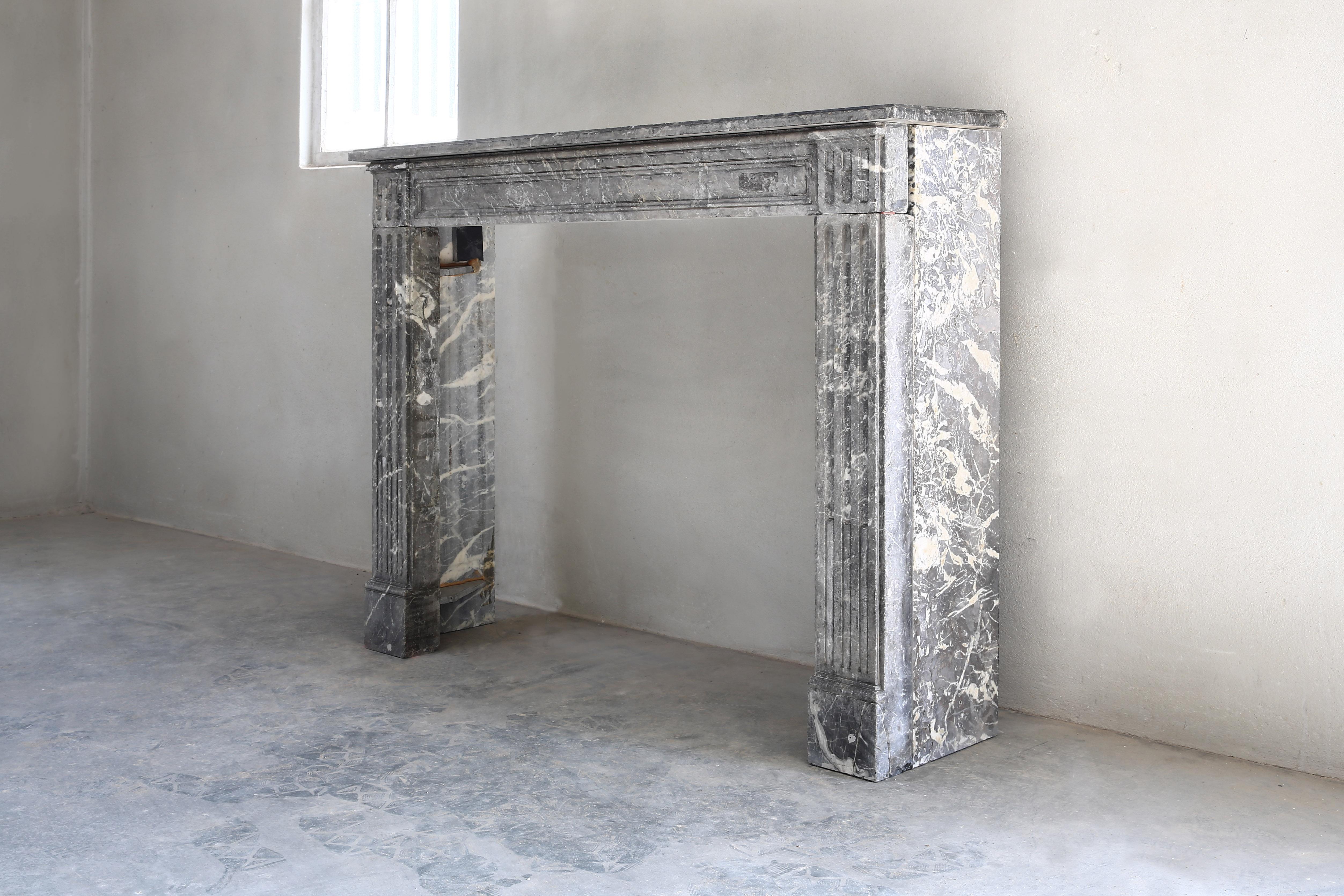 Beautiful antique mantelpiece of Gris de Ardenne marble in the style of Louis XVI from the 19th century. A straight shape and a beautiful type of marble, top has beautiful lines with flutes that also extend on the legs.