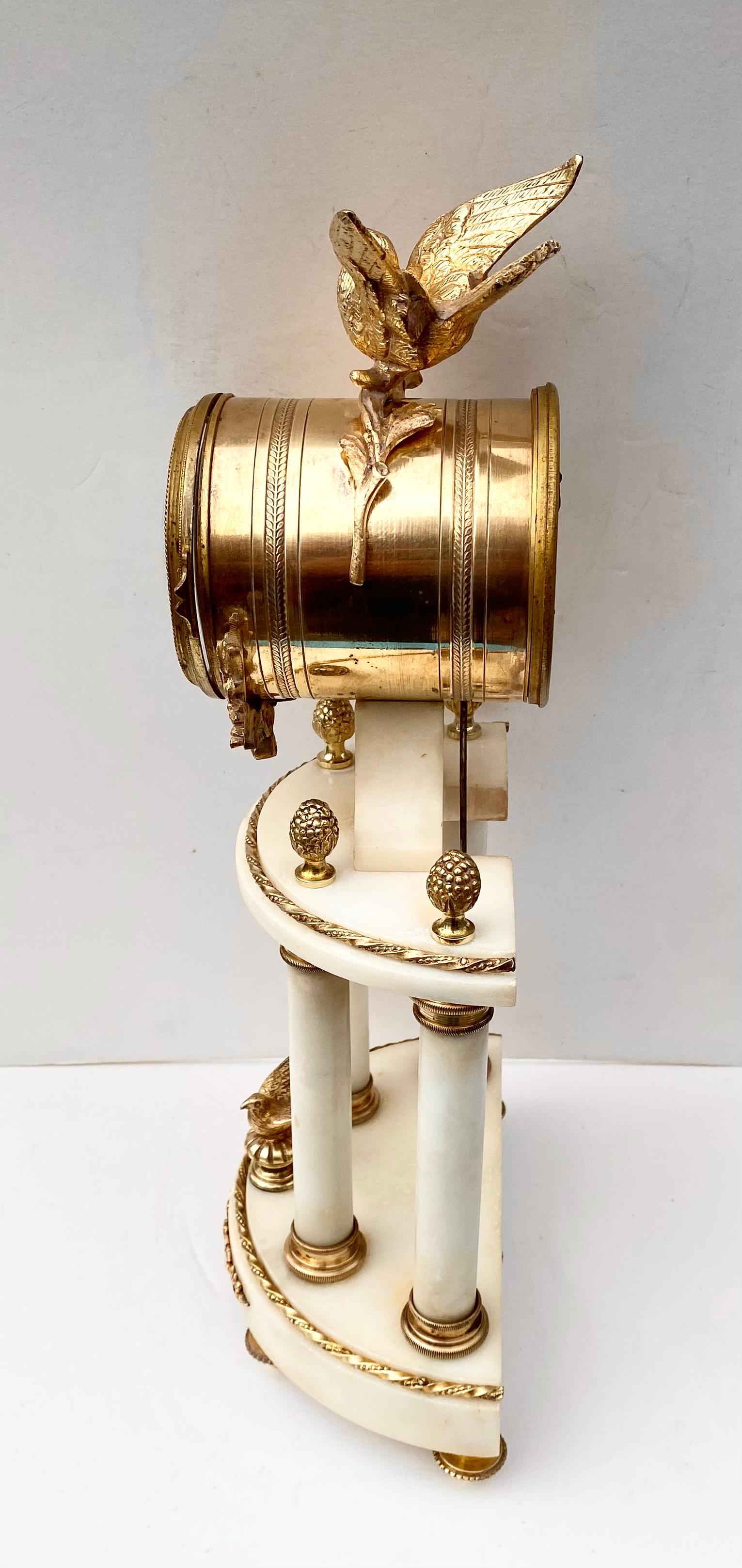An antique Louis XVI style clock in white marble and gilded bronze.

The clock rests on four small beaded bronze feet   There are four smooth cylindrical columns in white marble, embellished with gilded bronze beaded capitals that support demi-lune