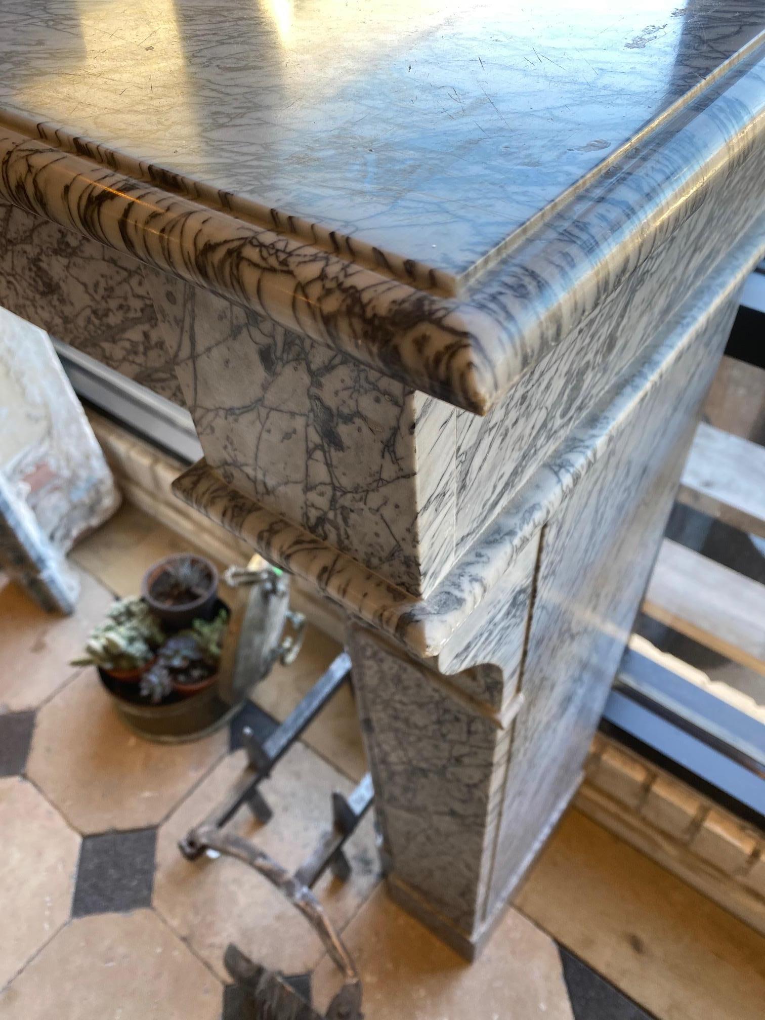 Louis XVI style “Marble Gris” mantel having a molded rectangular shelf above a simple frieze ending in outset and unadorned block ends, raised on rectangular supports headed by fluted corbels and terminating in square block feet.
Dimensions from