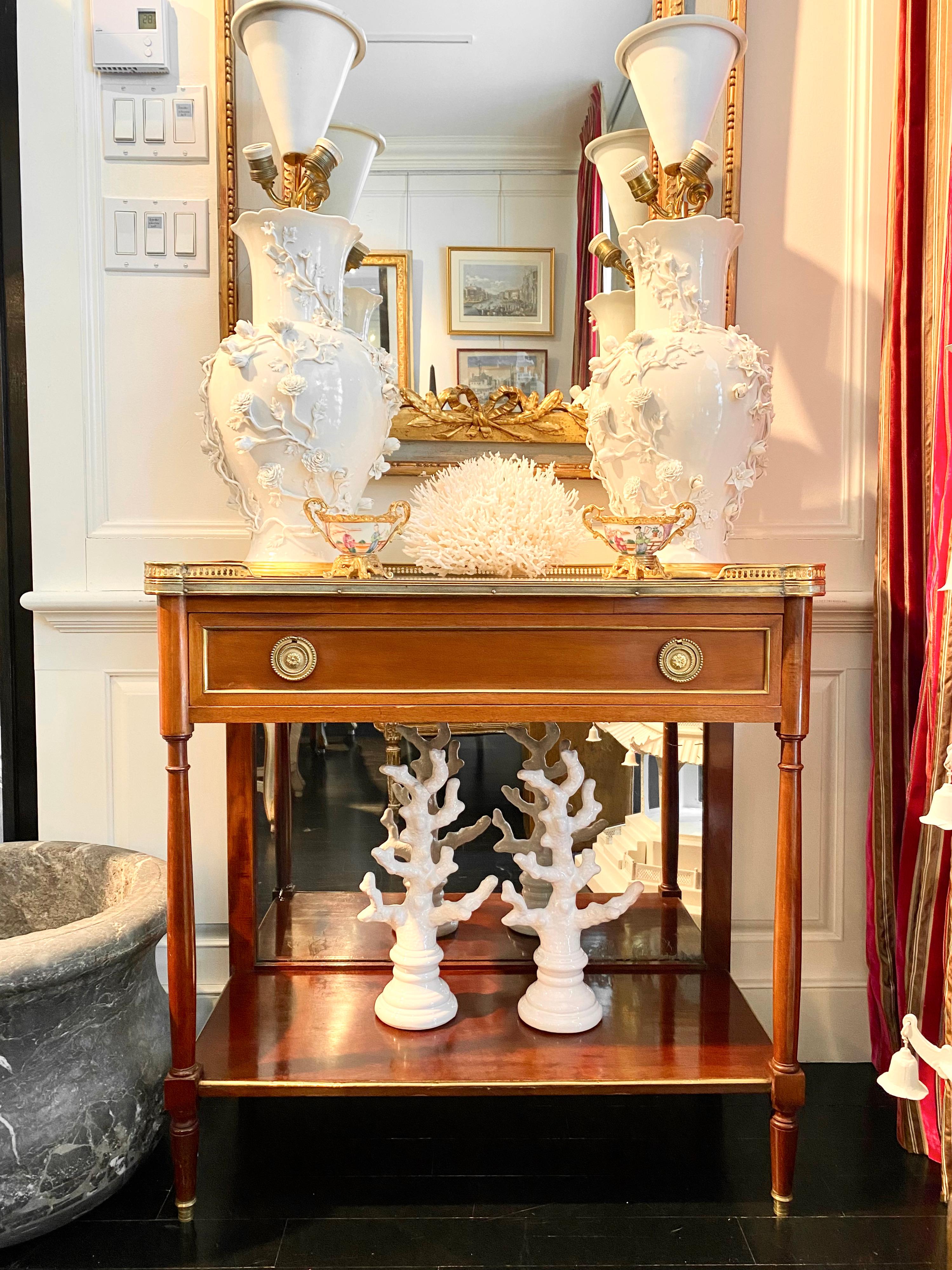Louis XVI style, marble top console, bronze gallery, mirror back
Long single top drawer and bottom shelf mounted on four legs with bronze sabot caps. White marble top with circular corners surrounded by a bronze pierced gallery. Gilt bronze