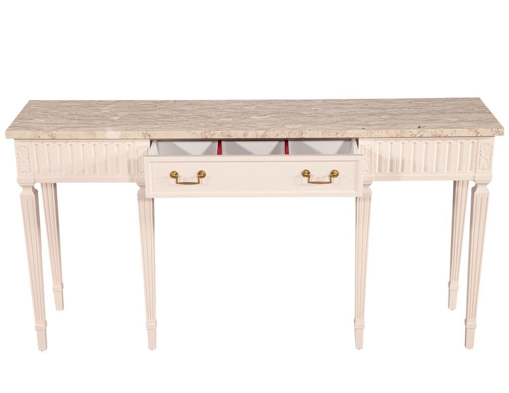 Louis XVI Style marble top console table. This 1940’s American piece is fully restored in a light bubble gum lacquer finish with original brass hardware. Beautiful beige crackle marble with unique detailed veining. Complete with small storage drawer