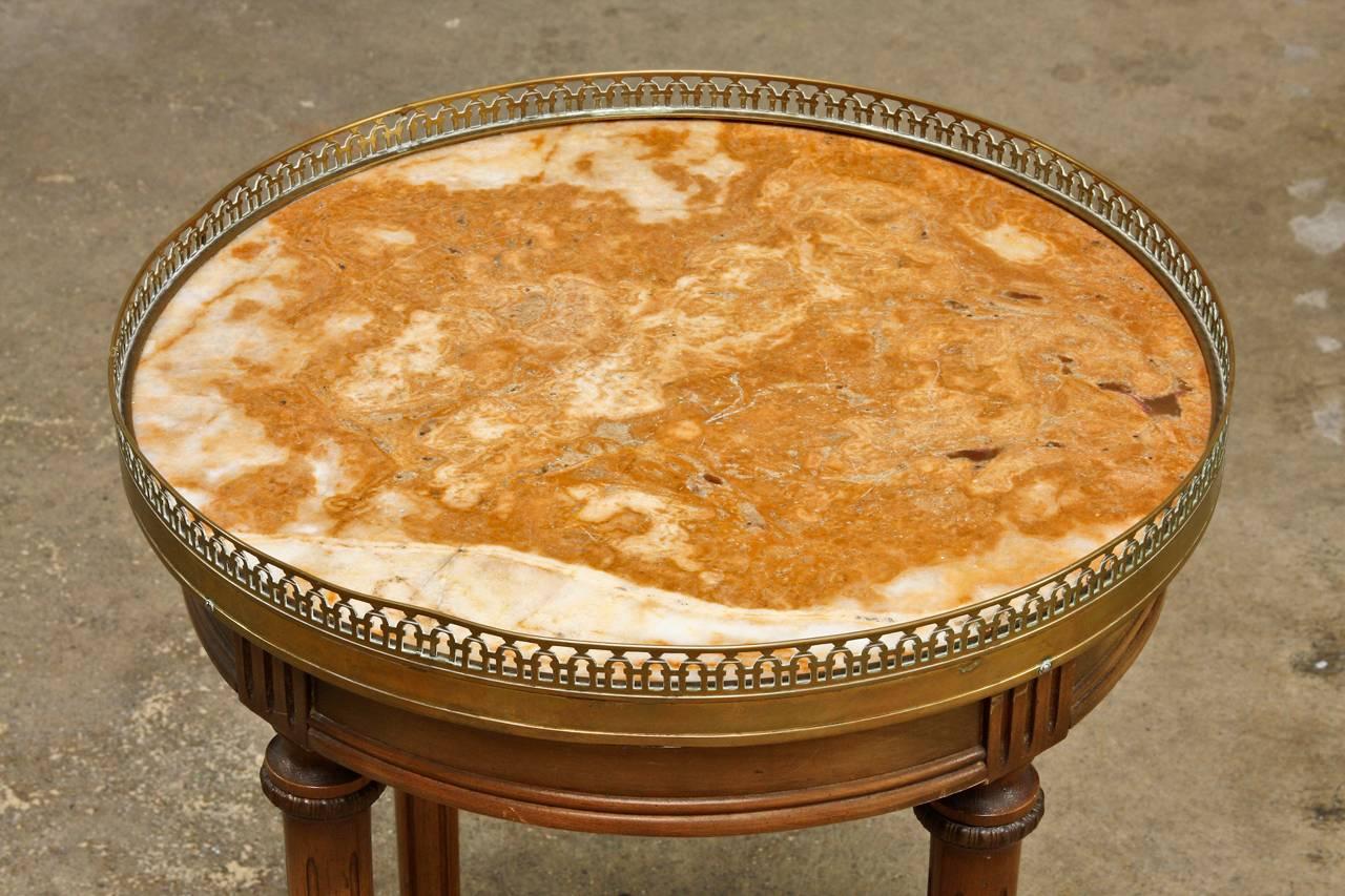 Fabulous little marble-top gueridon drink table carved from mahogany made in the neoclassical Louis XVI style. Having a decorative pierced brass galleried round top with a colorful marble inset. Supported by four fluted legs ending with brass