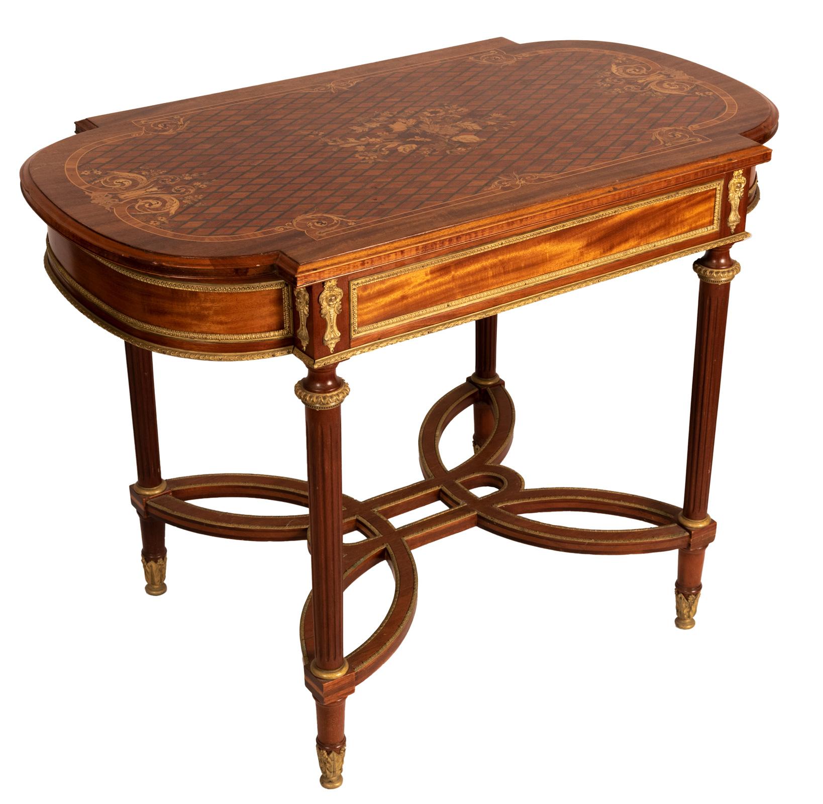 A Louis XVI style marquetry table with the top decorated with intricate floral sprays made of exotic woods, the table mounted with ormolu and fluted columnar legs connected with orbicular stretchers, (circa 1880).