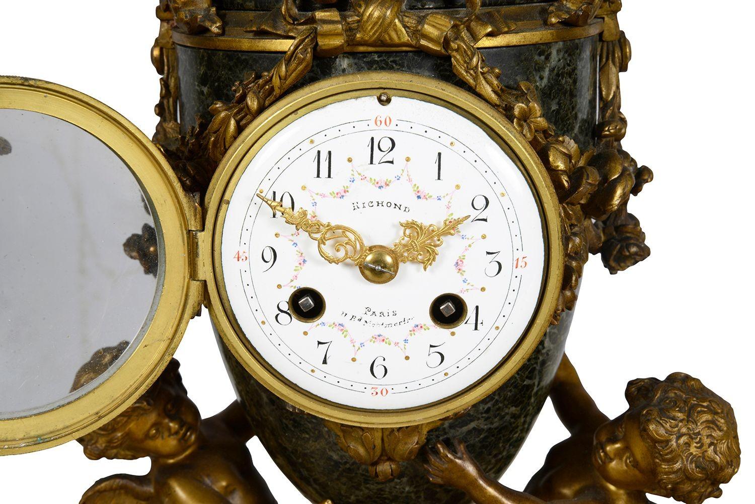 Dieses exquisite französische Uhrenset aus dem 19. Jahrhundert besticht durch die Kombination von vergoldetem Ormolu und grünem Marmor. Das Herzstück der Uhr ist elegant mit aufwändigen vergoldeten Details verziert, darunter Engelsfiguren, die den