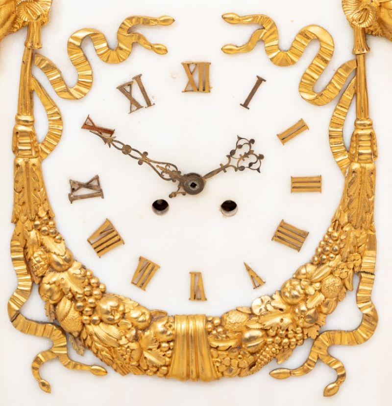 Louis XVI Style Ormolu Mounted White Marble Clock, 19th century, the tapering marble block mounted with a frieze and ram's heads issuing foliate and fruit swags, centered by the dial, the movement strike on bell, on a rectangular stepped plinth. 19