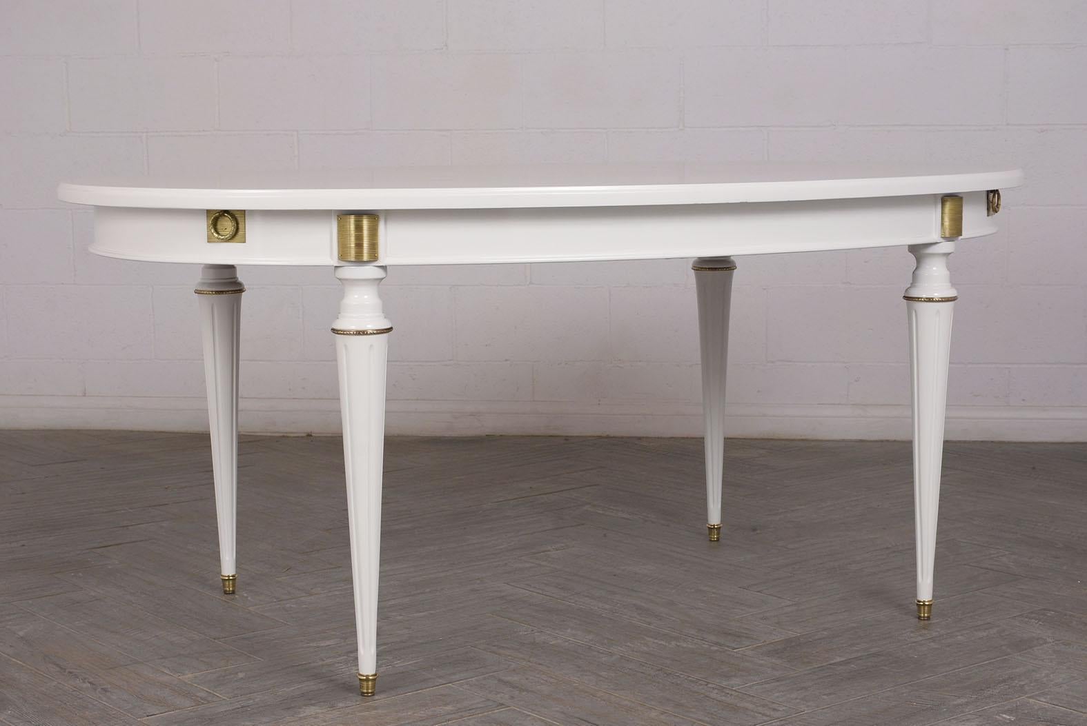 This Louis XVI style oval dining table has a beautiful stained in white color with a lacquered finish. It also features brass moldings and accents around the top and carved legs. The table comes with two extra leaves. The table is in great condition