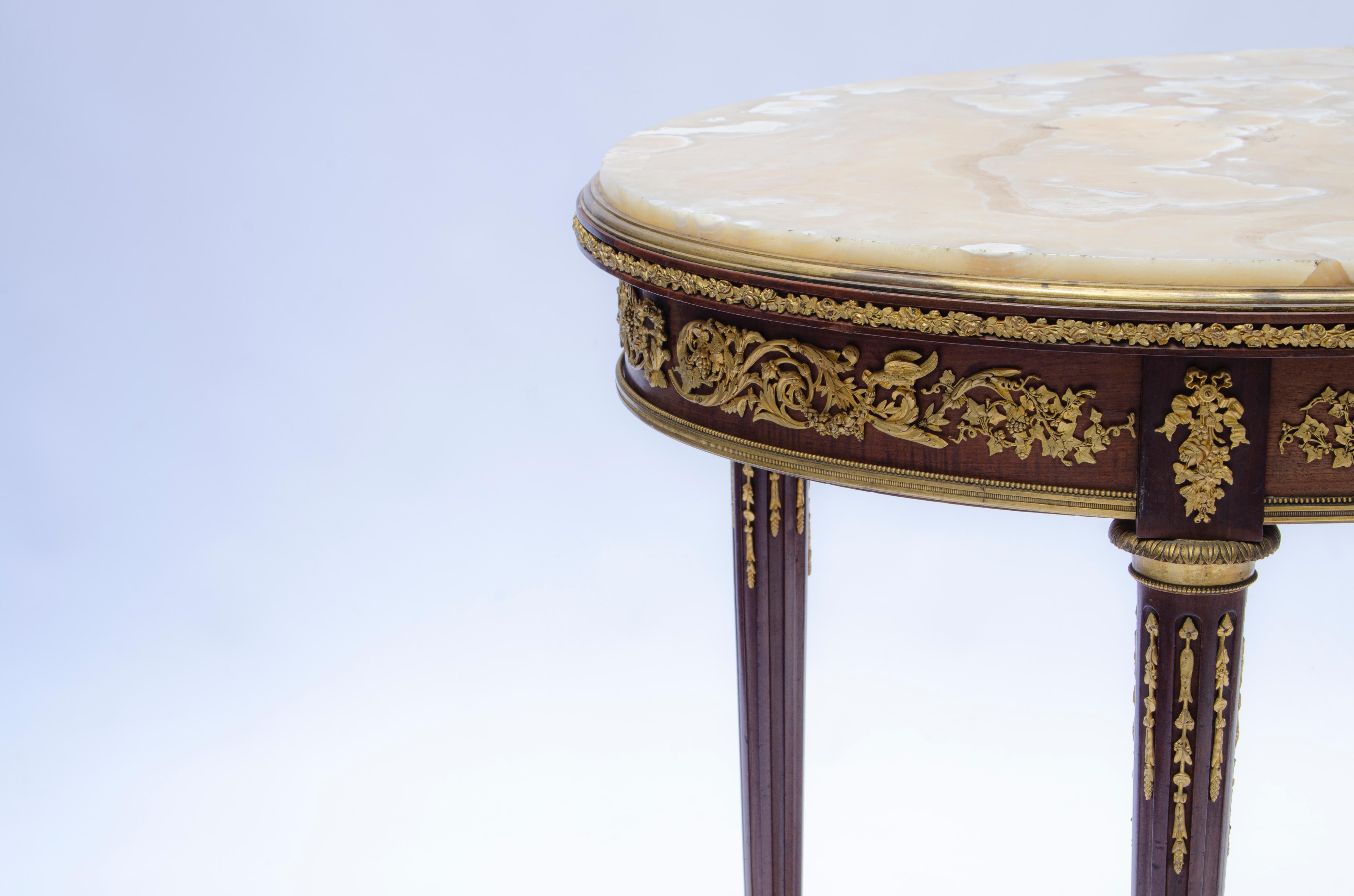 Table d'appoint ovale française, de style Louis XVI, en bois d'acajou et bronze doré (Ormolu), montée sur guéridon et plateau en marbre. Dans son design, on peut distinguer qu'il est entouré de guirlandes de bronze dans sa partie supérieure. Sur ses