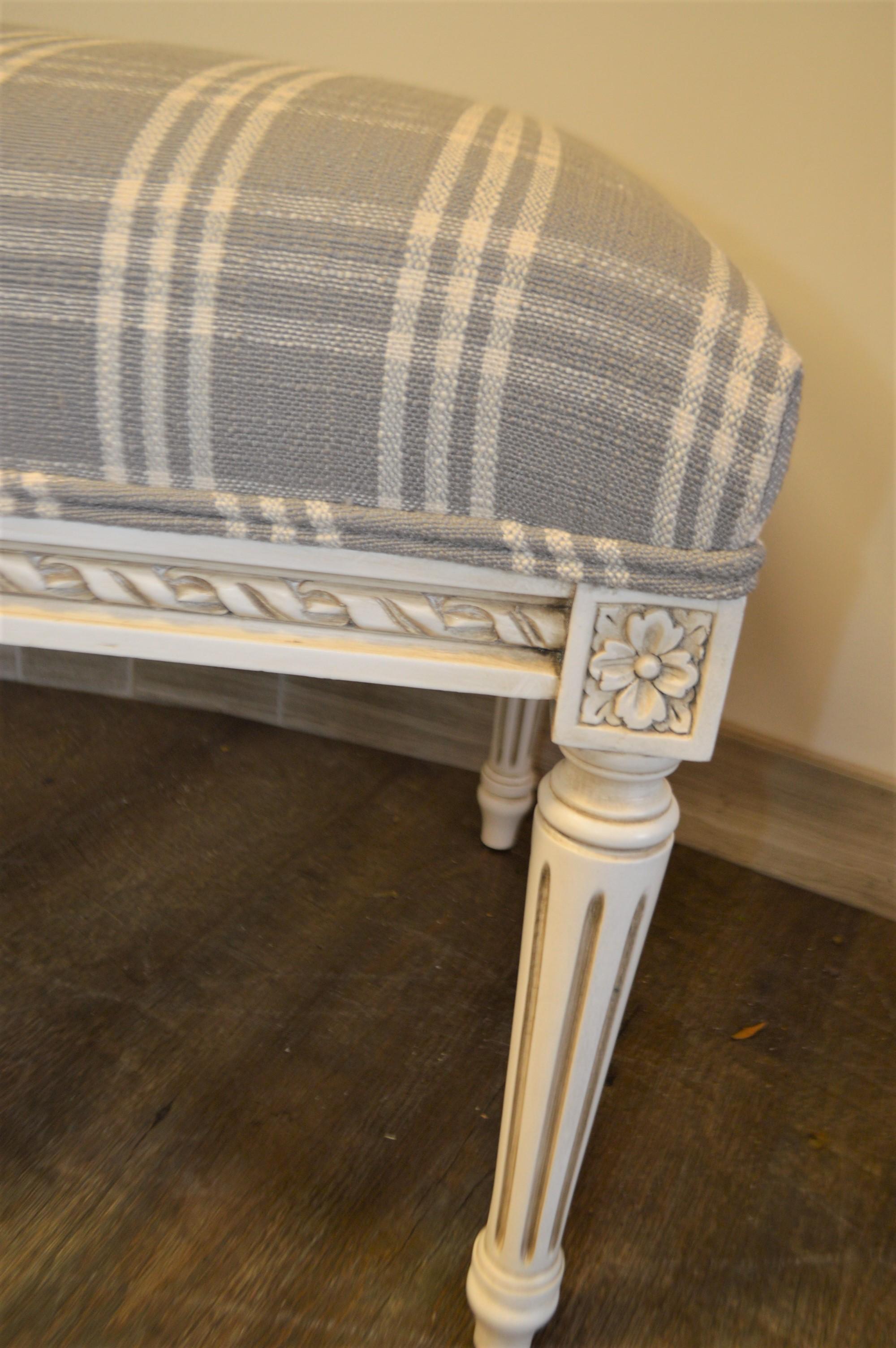 Louis XVI style painted bench with attractive carving details on all 6 legs as well as the ribbon carving all around the apron.
It has been upholstered with a charming fabric in a grey and off-white plaid over a medium firm foam.
This bench is