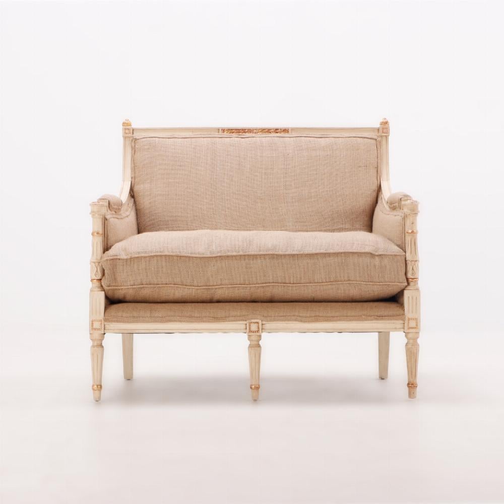 Sillón marqués de estilo Luis XVI pintado y dorado C 1950. Esta cómoda silla de armazón de madera, llamada marquesa por su amplio asiento y su respaldo bajo y acampanado, tiene una cresta tallada con motivos foliados, flanqueada por remates