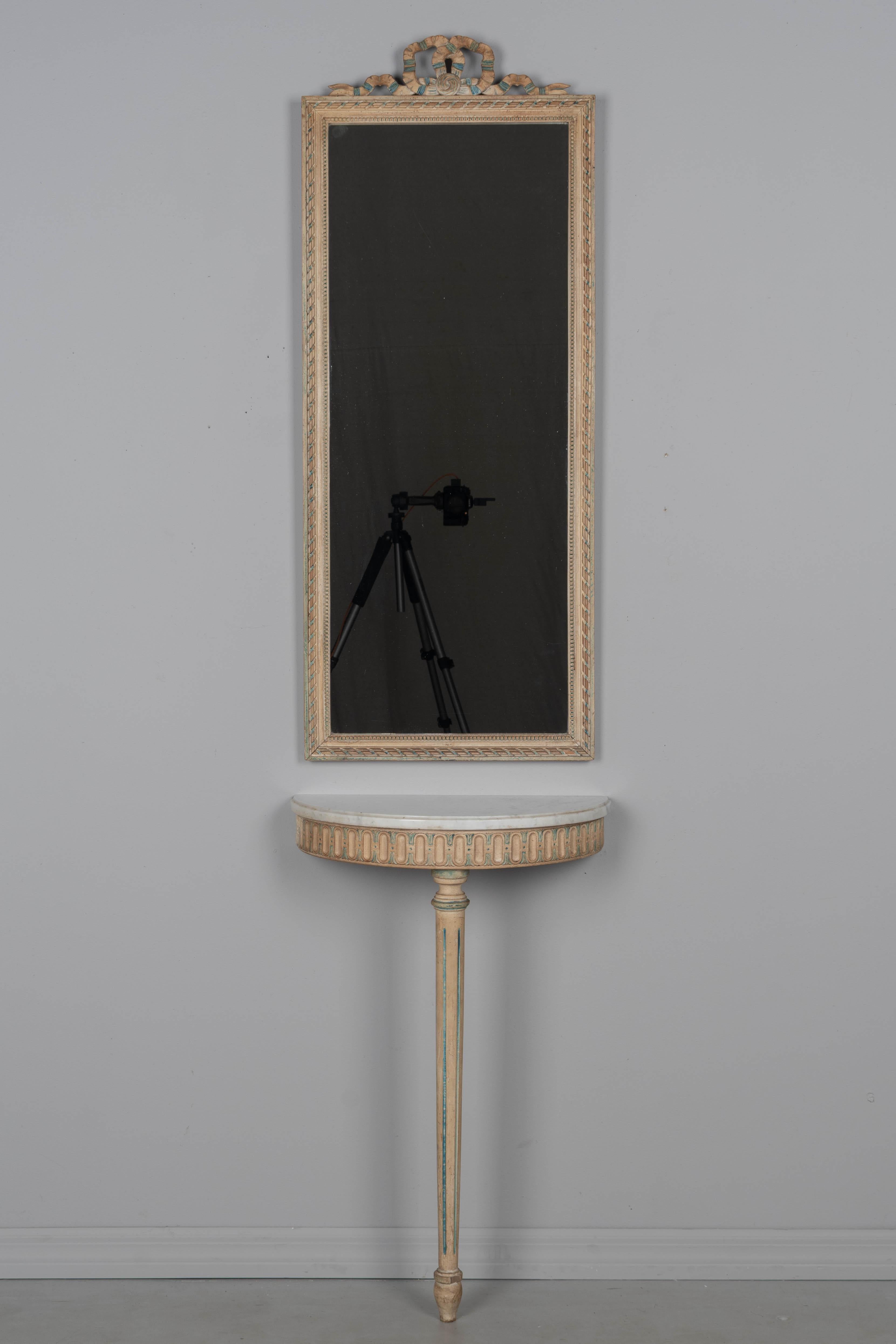A Louis XVI style French polychrome painted mirror with matching demilune console table. Nice tall proportions with carved bow detail. Console has removable white marble top and will need to be fastened to the wall. Good condition with minor paint