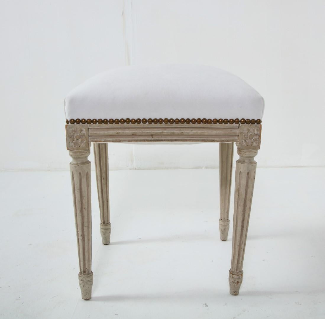 Painted wood footstool/bench, Louis XVI style, c. 1930. Top is newly upholstered in Kravet Carmine in Cloud, with brass nail head detail. 

Louis XVI style furniture is identified by its restrained lines and less ornamental tendencies as compared