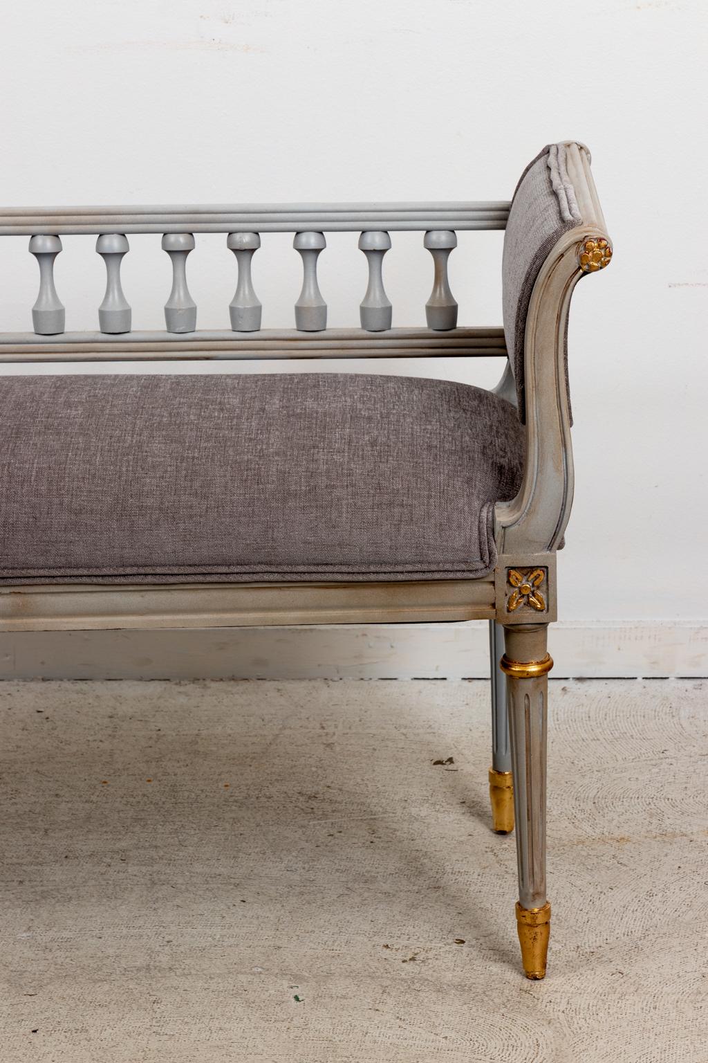 Circa 1960s Louis XVI style painted gilded bench with turned spindles and scrolled arms, newly upholstered with some wear to finish. Made in the United States. Please note of wear consistent with age.