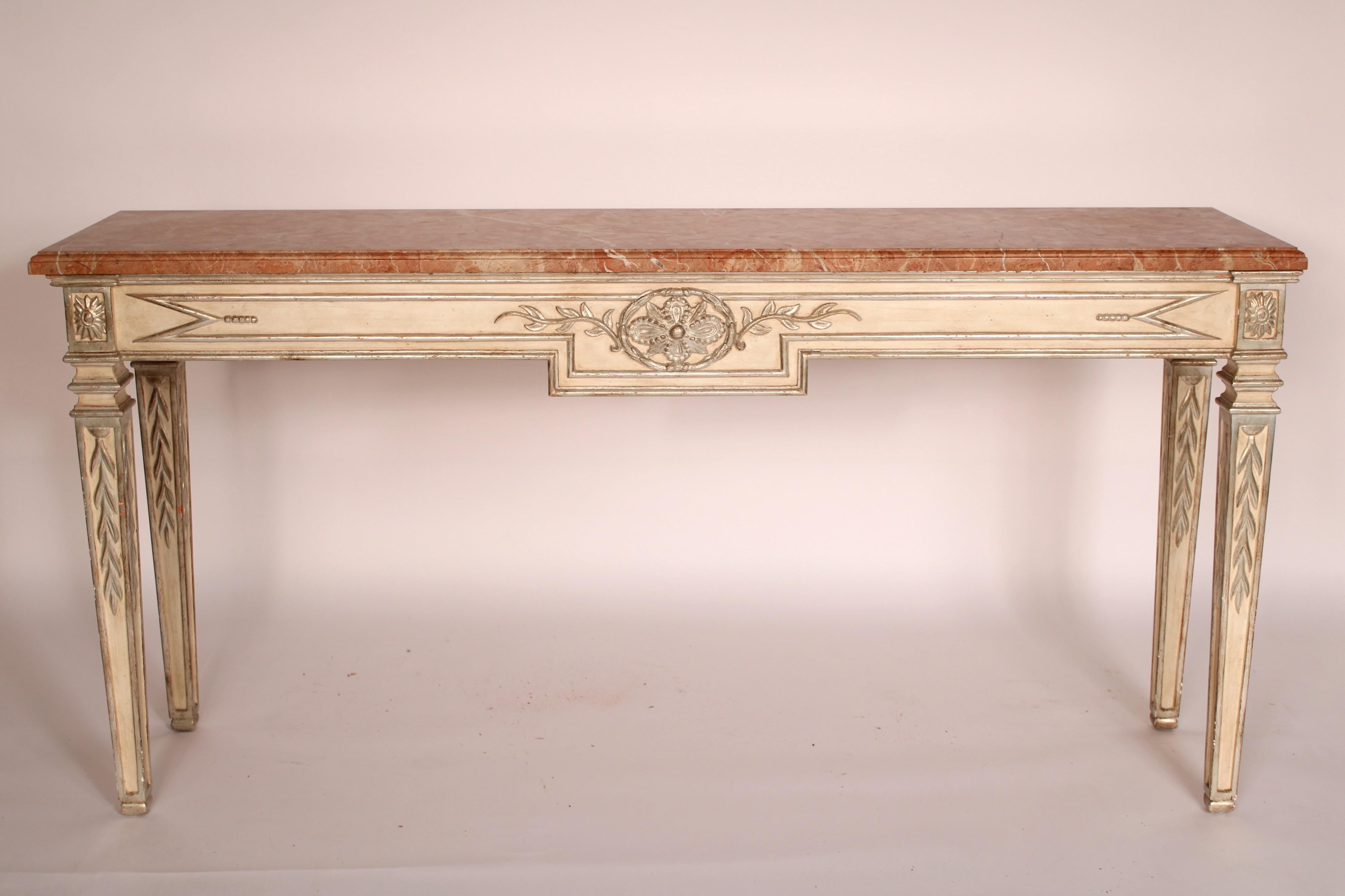 Louis XVI Style painted and silver leafed marble top console table, late 20th century. With a pink marble top with molded front and side edges, a frieze with a central medallion and vine decoration, top of each leg with silver leaf patera, legs are