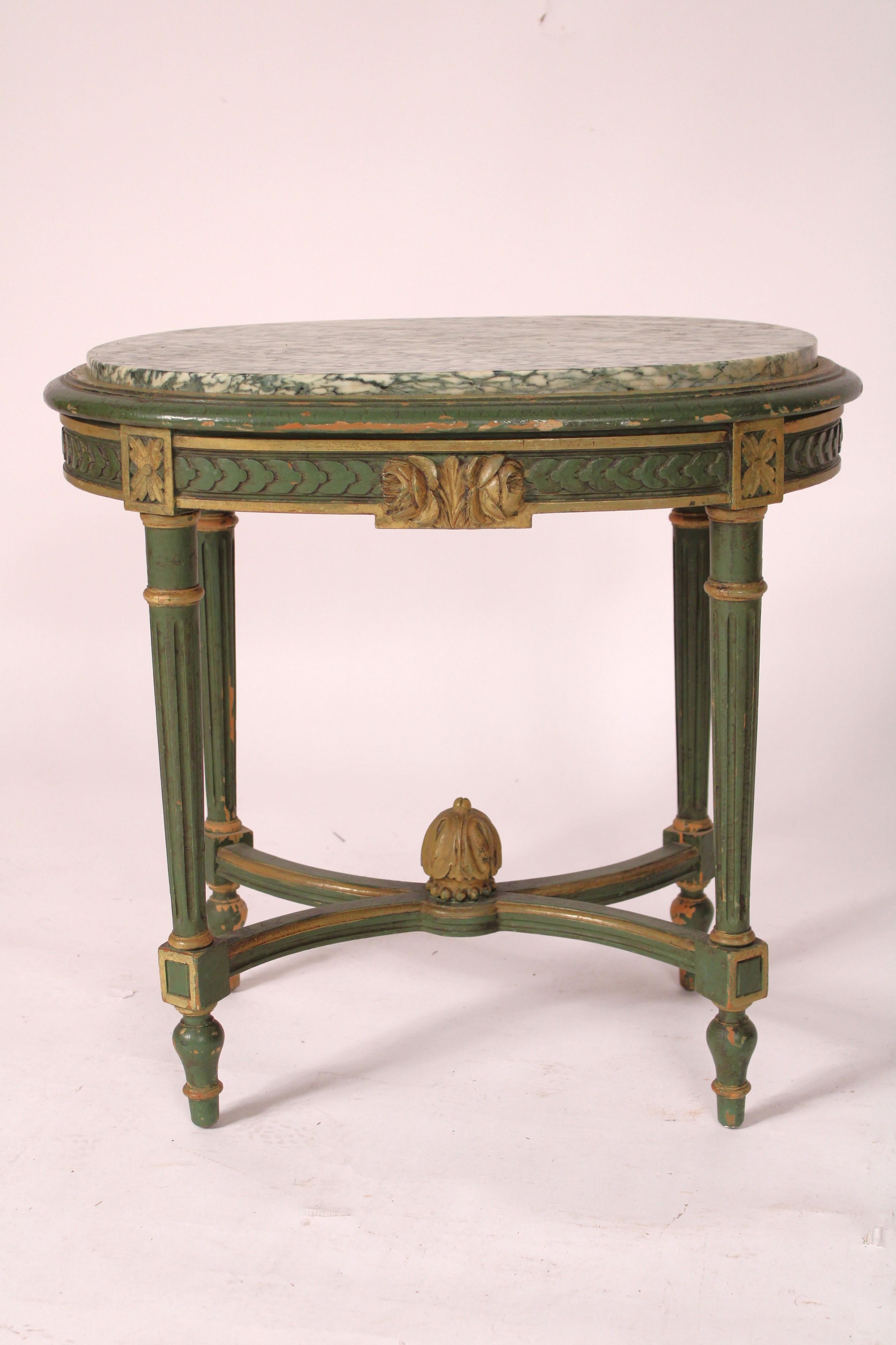 Table d'appoint ovale de style Louis XVI, peinte en vert, avec un plateau en marbre vert et blanc, vers les années 1920. Plateau en marbre vert et blanc, frise guillochée, pieds tournés, fuselés et cannelés se terminant par des pieds toupies, reliés