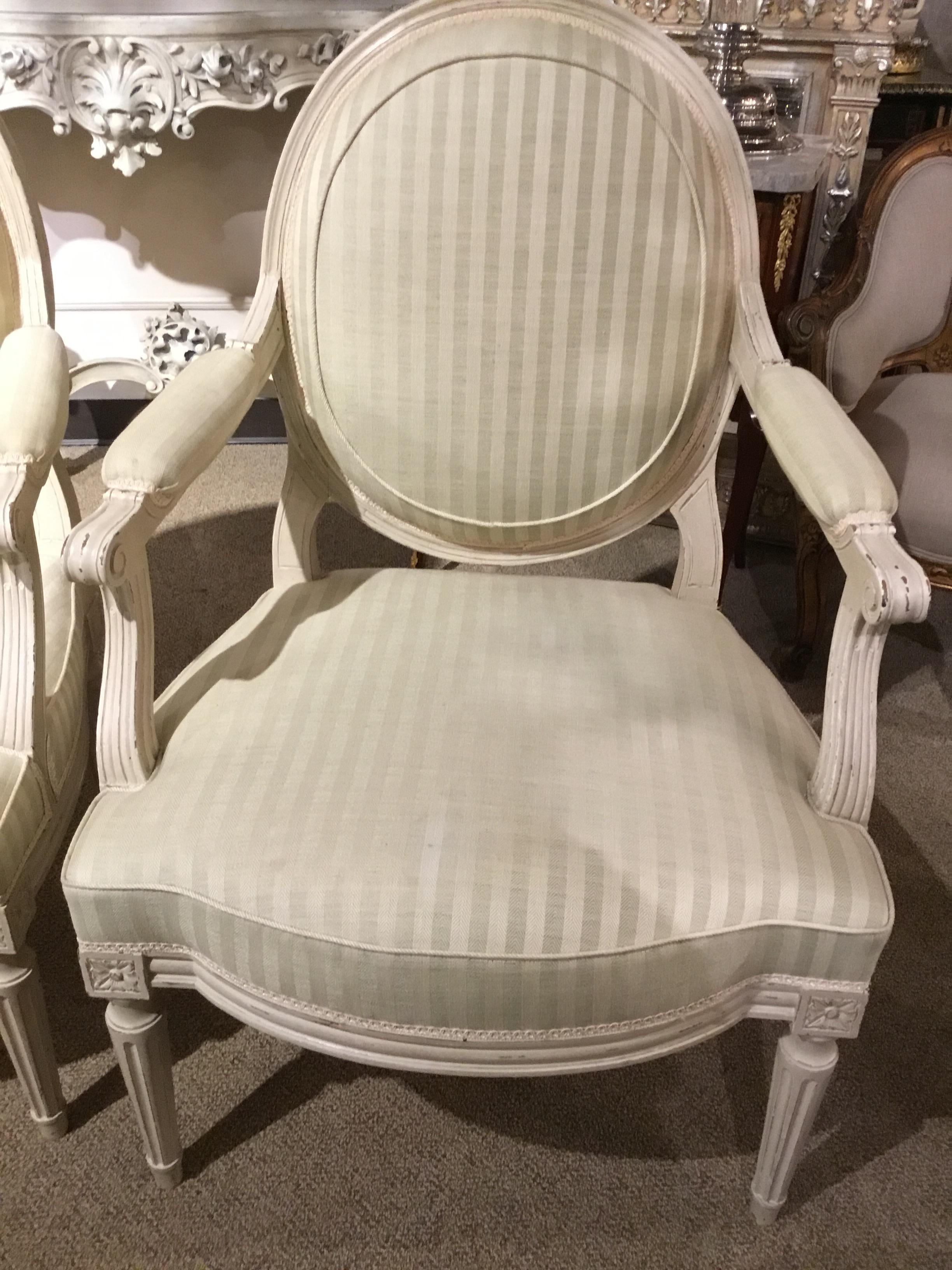 Louis XVI style chairs in white painted finish having an oval shaped back.
White and cream striped fabric. Reeded legs
Painted in a faux artistic distressing finish.