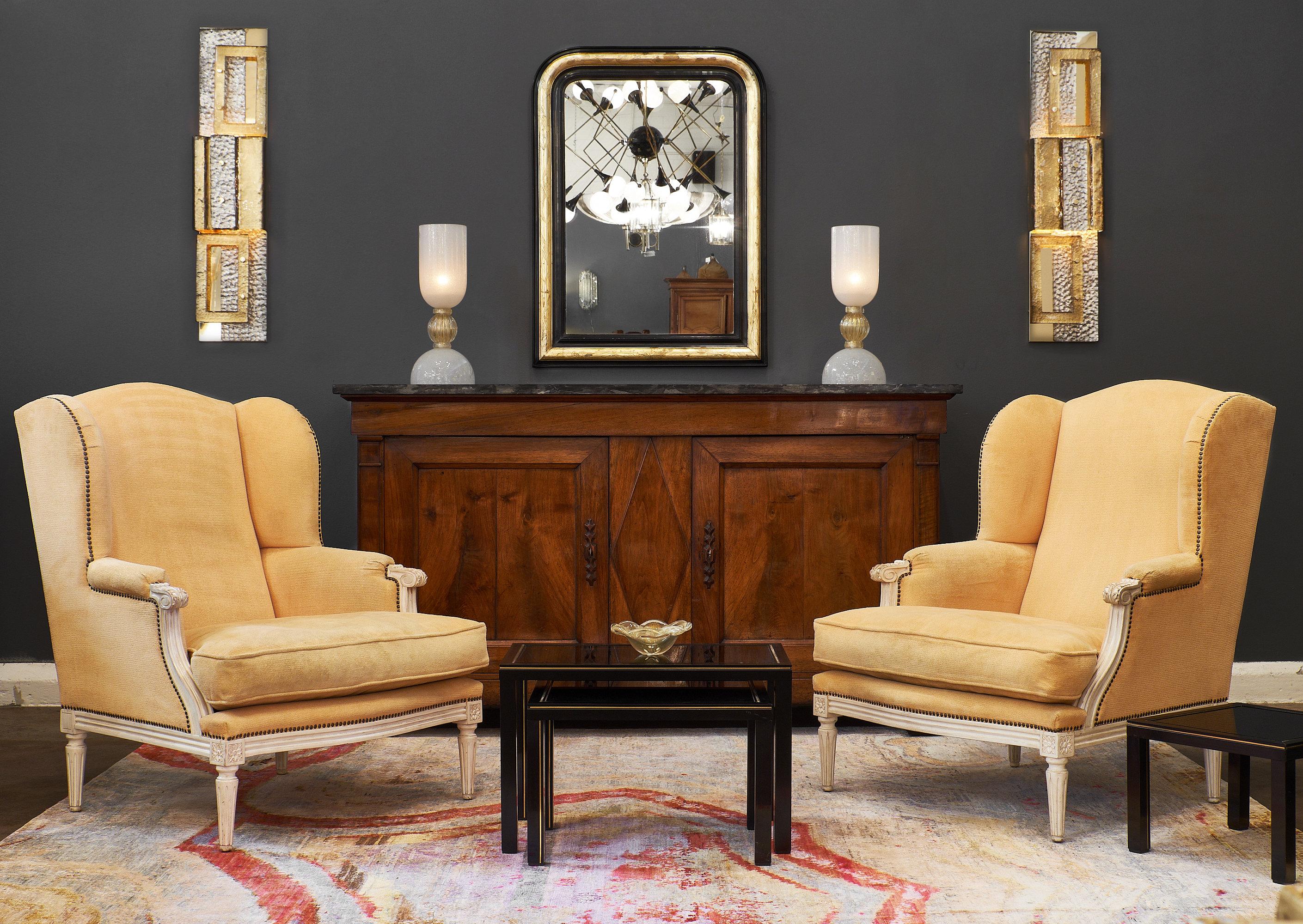 A pair of yellow Louis XVI style “Bergères a Oreilles” featuring the original hand-carved frames and paint. The original upholstery is in an original gold velvet fabric in decent condition with brass nailheads. We couldn’t resist the comfortable,