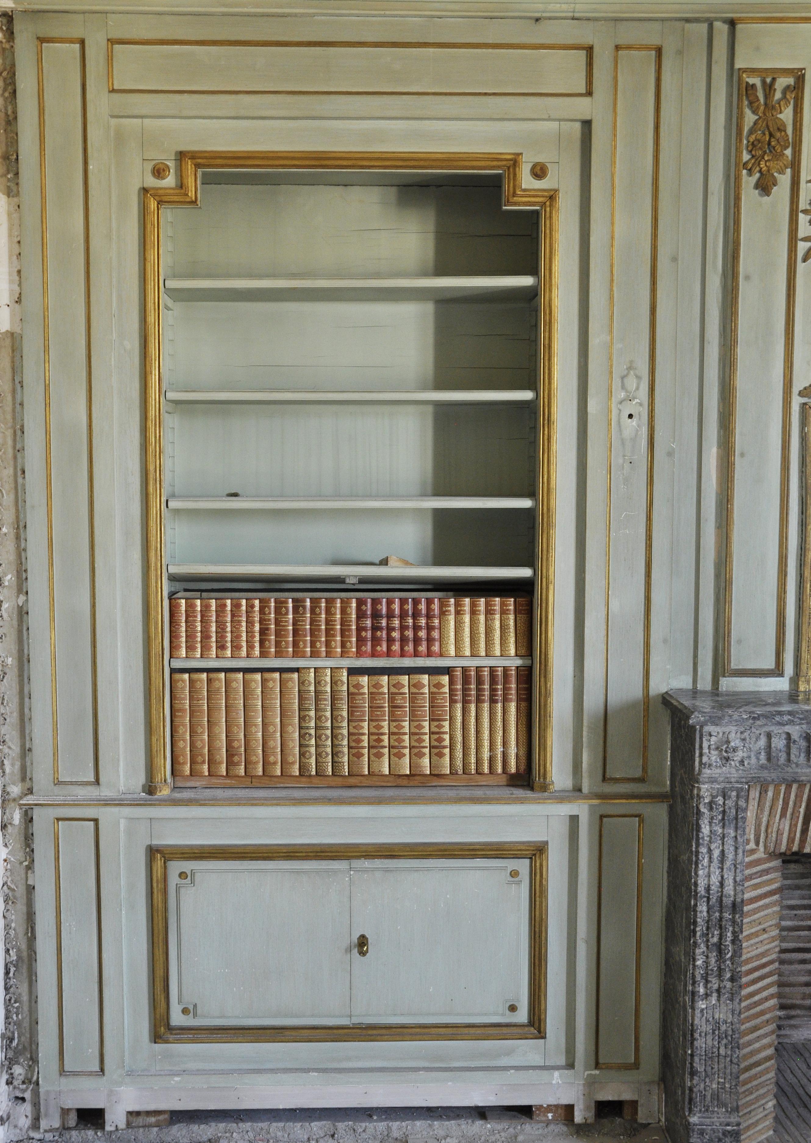 Dieses getäfelte Zimmer im Stil Louis XVI besteht aus zwei Regalen und Schränken mit Flügeltüren aus hellgrün gestrichenem Holz aus dem 20. Jahrhundert.
Sie umrahmen einen Kaminsims aus grauem Marmor Saint-Anne aus der Zeit Ludwigs XVI. mit