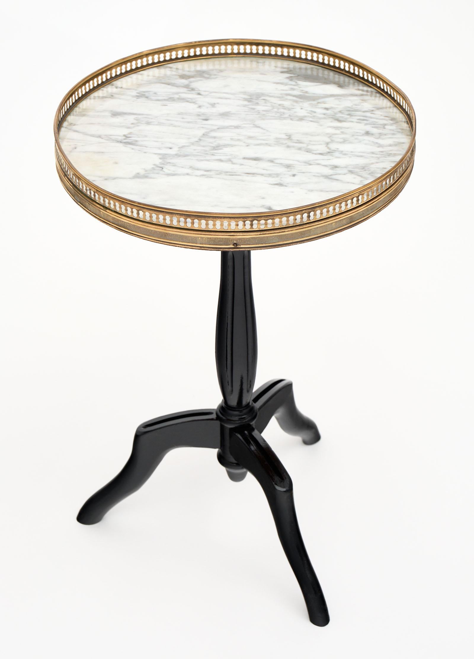 Louis XVI style petite side table with a mahogany base that has been ebonized and finished with a French polish. We love the fluted tulip center foot and tripod feet. The round top is original Carrara marble and is finished with a brass gallery. A
