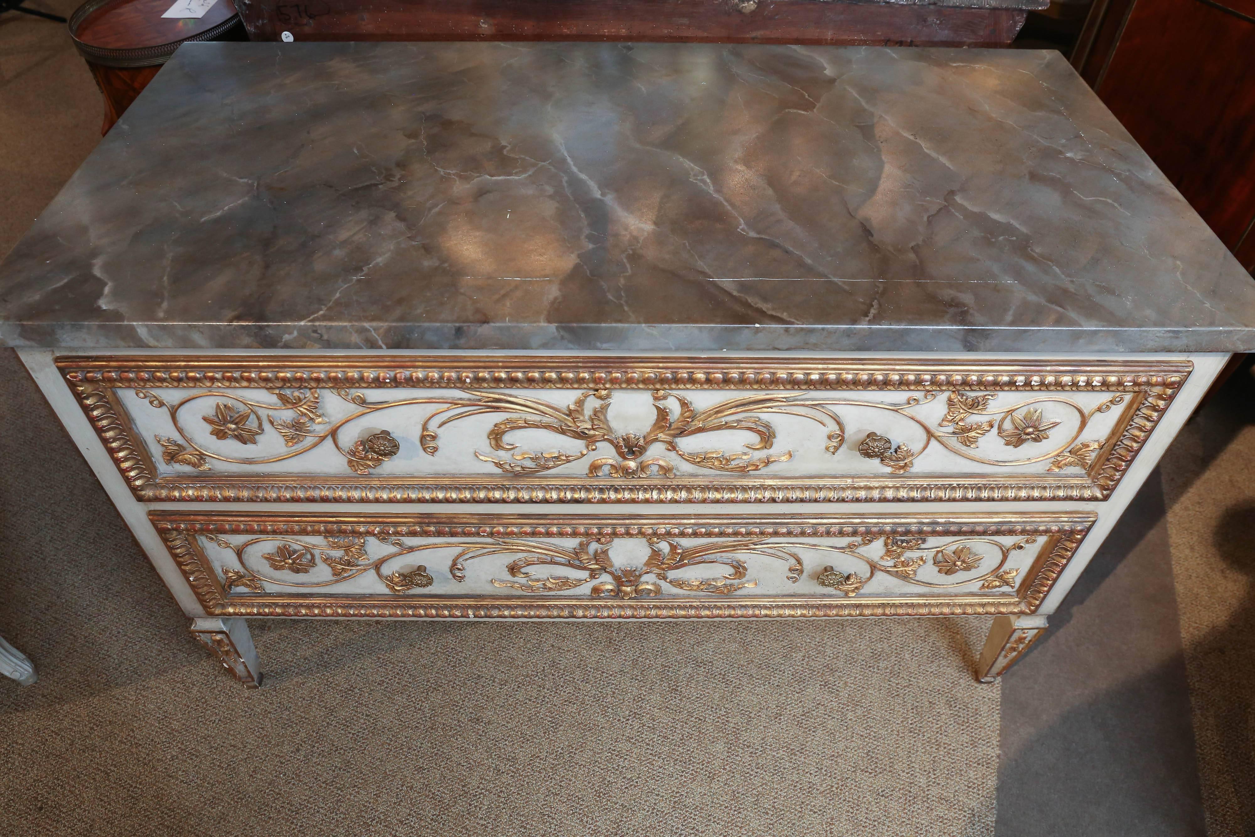 The rectangular faux marble top is above a conforming case fitted with two
long drawers, both paneled and with gilt scrolling foliate accents, the sides
with the same designs, raised on paneled and bellflower-carved tapering
square legs.