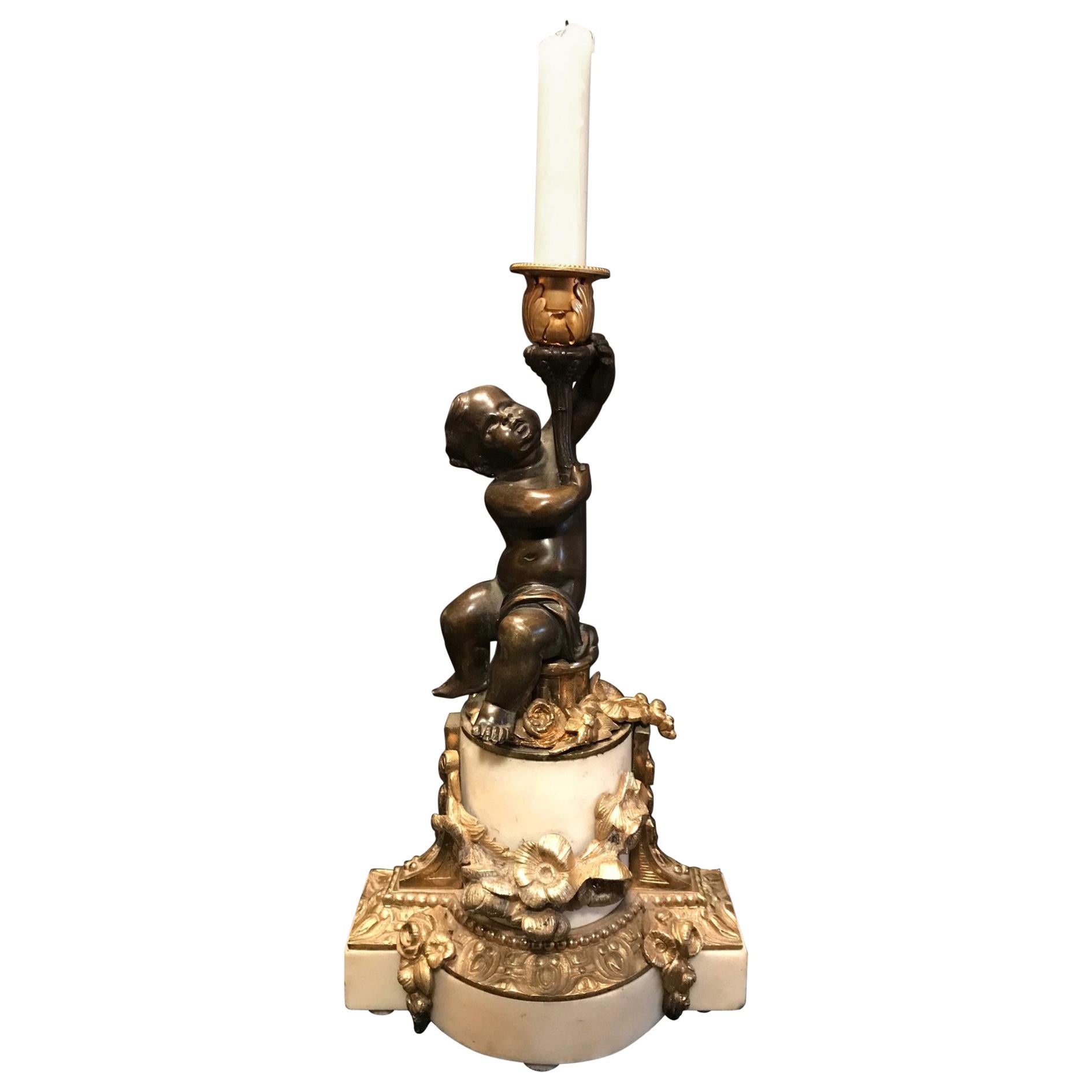 This French candleholder, in the style of Clodion, is mounted on white statuary Carrara marble. The patinated putto holds a candle support of flowering acanthus leaves. Circular and rectangular marble shapes combine to create the base which is well