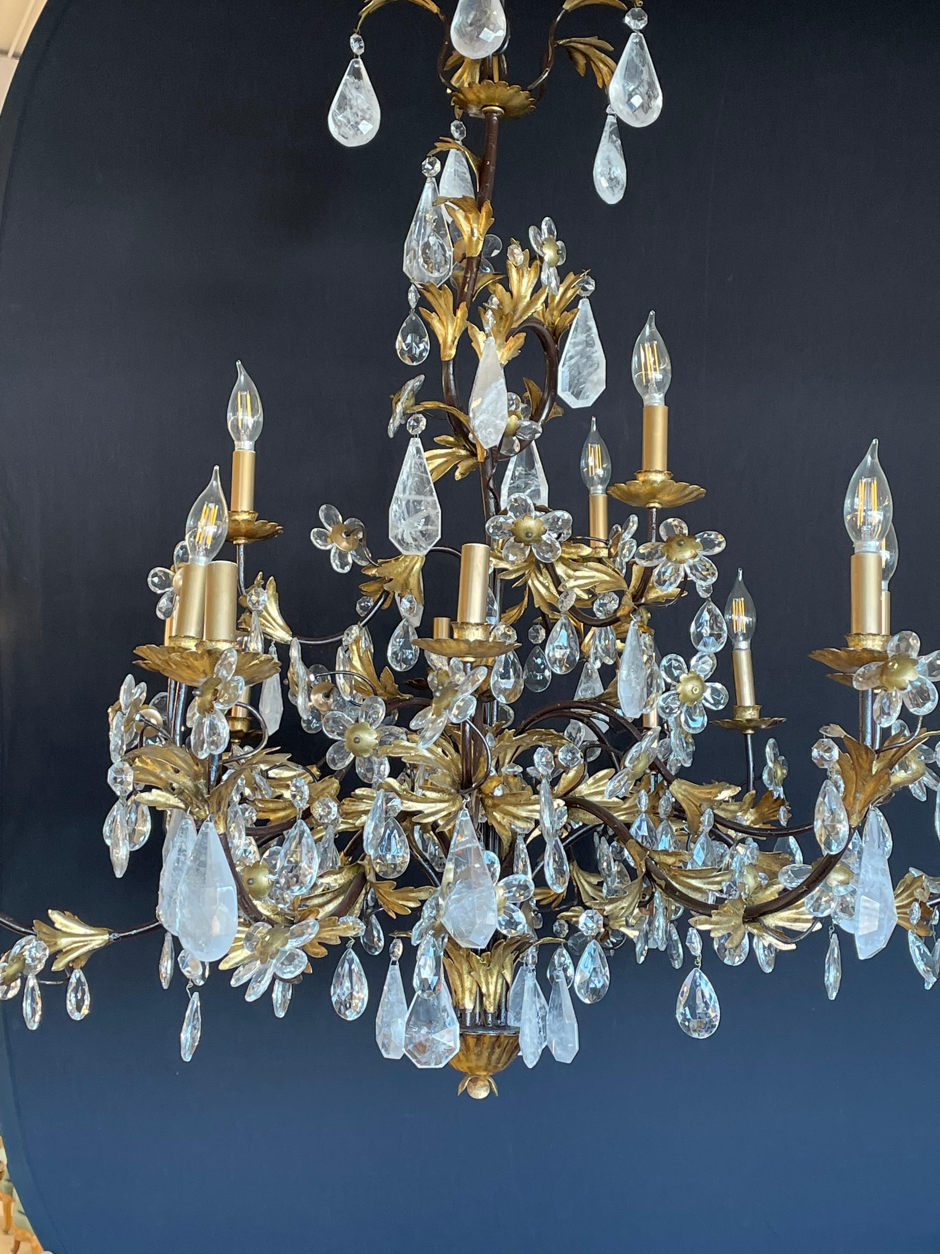 A Hollywood Regency or Louis XVI Style Chandelier having many large and impressive rock crystals prisms hanging from an ebony and gilt metal frame of floral, swag and large crystal roses. This finely craft stunning chandelier is not served well by