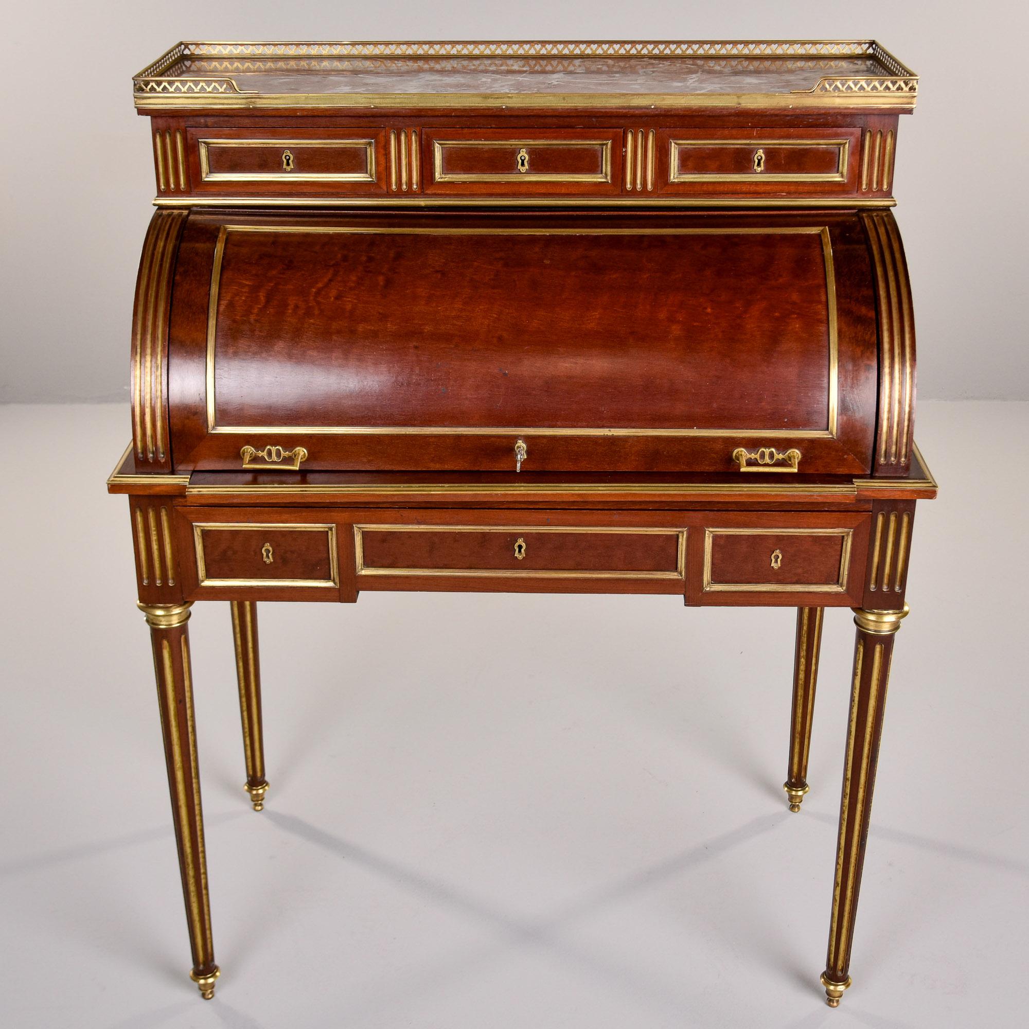 Found in France, this Louis XVI style roll top cylinder desk dates from approximately 1920. The desk is mahogany with brass fittings. There is a marble inset top with brass gallery with three locking drawers below. Inside the roll top are three more