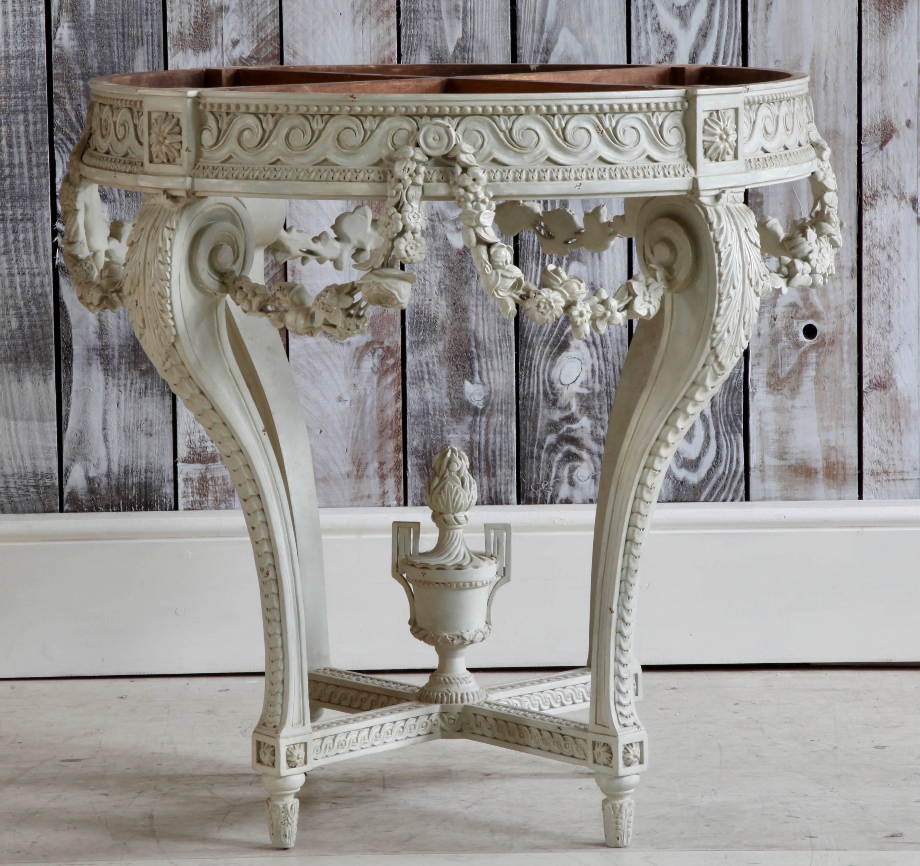 Round console table hand-carved in solid wood in the Louis XVI style featuring neoclassical decorative borders and finely carved floral swags draped in swathes around the tabletop with acanthus leaves at the top of scrolled legs and an urn at the