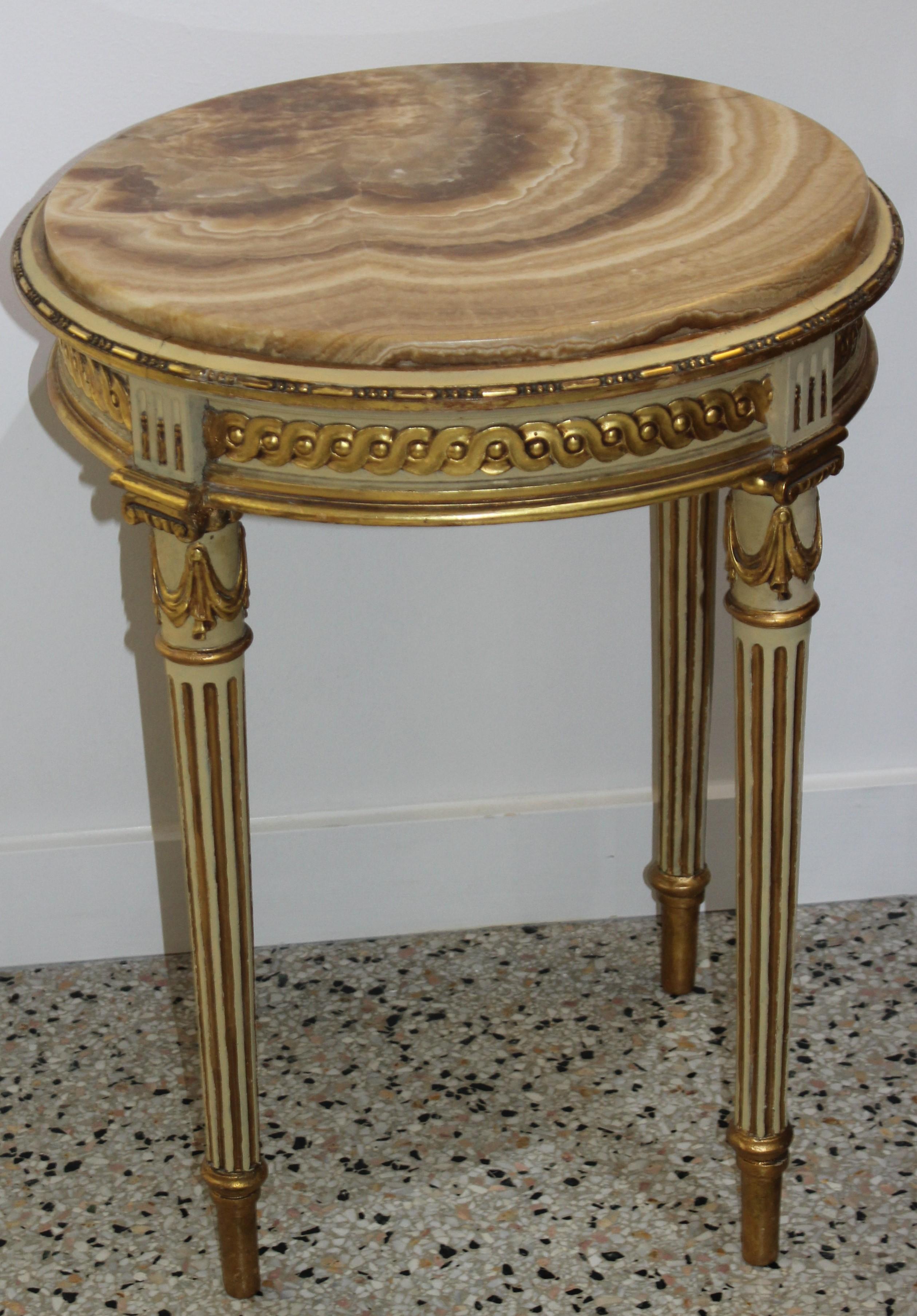 This stylish, romantic and chic petit side table was acquired from a Palm Beach estate. The table dates to the 1890s-1920s and is painted in a soft putty green and accented with gild gold. The butterscotch colored onyx inset comliments the gilt gold