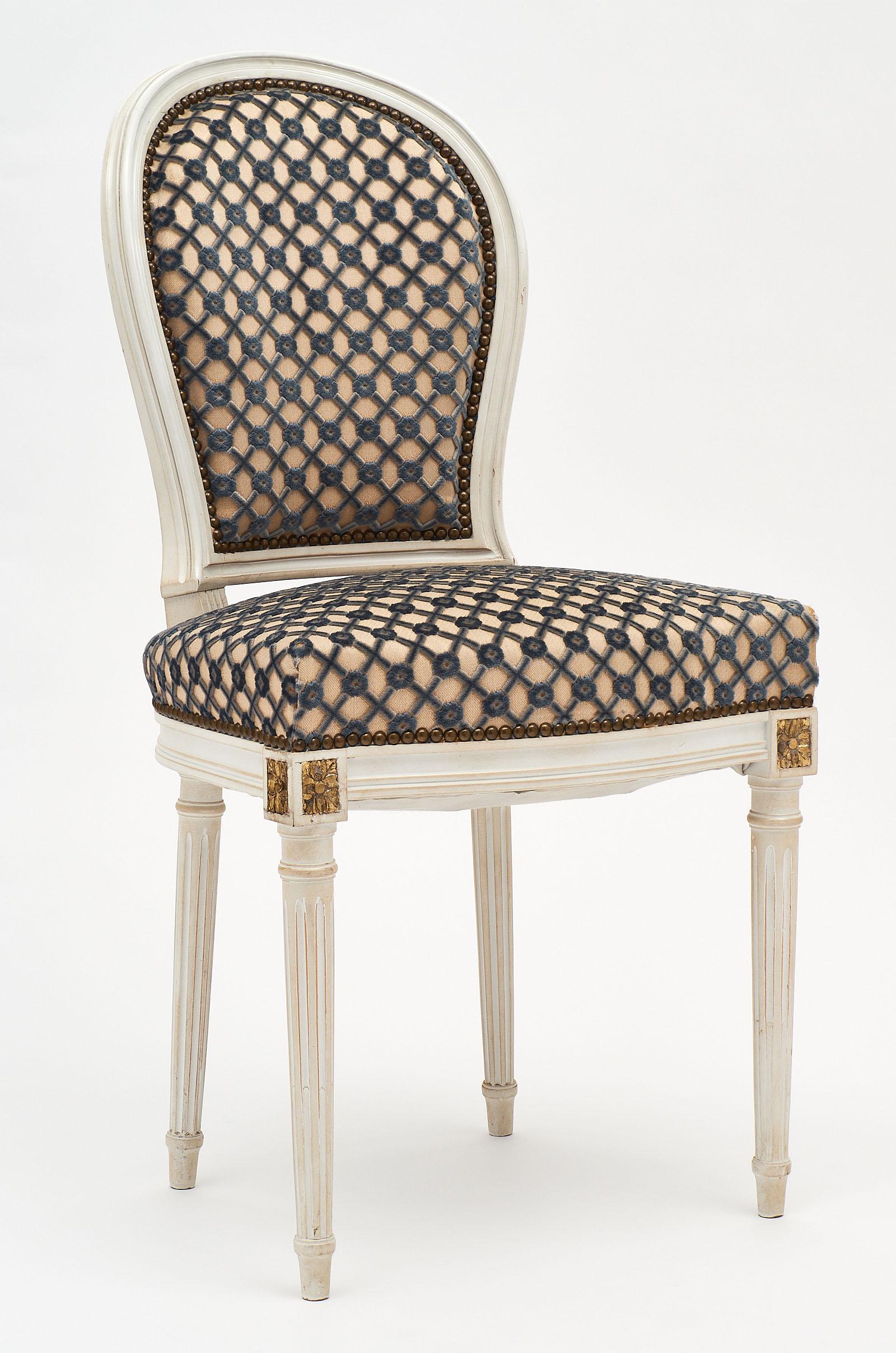 A set of four Louis XVI style chairs with medallion backs featuring hand carved details and gold-leaf accents. We love the Classic, painted frames. The upholstery is original to the set.