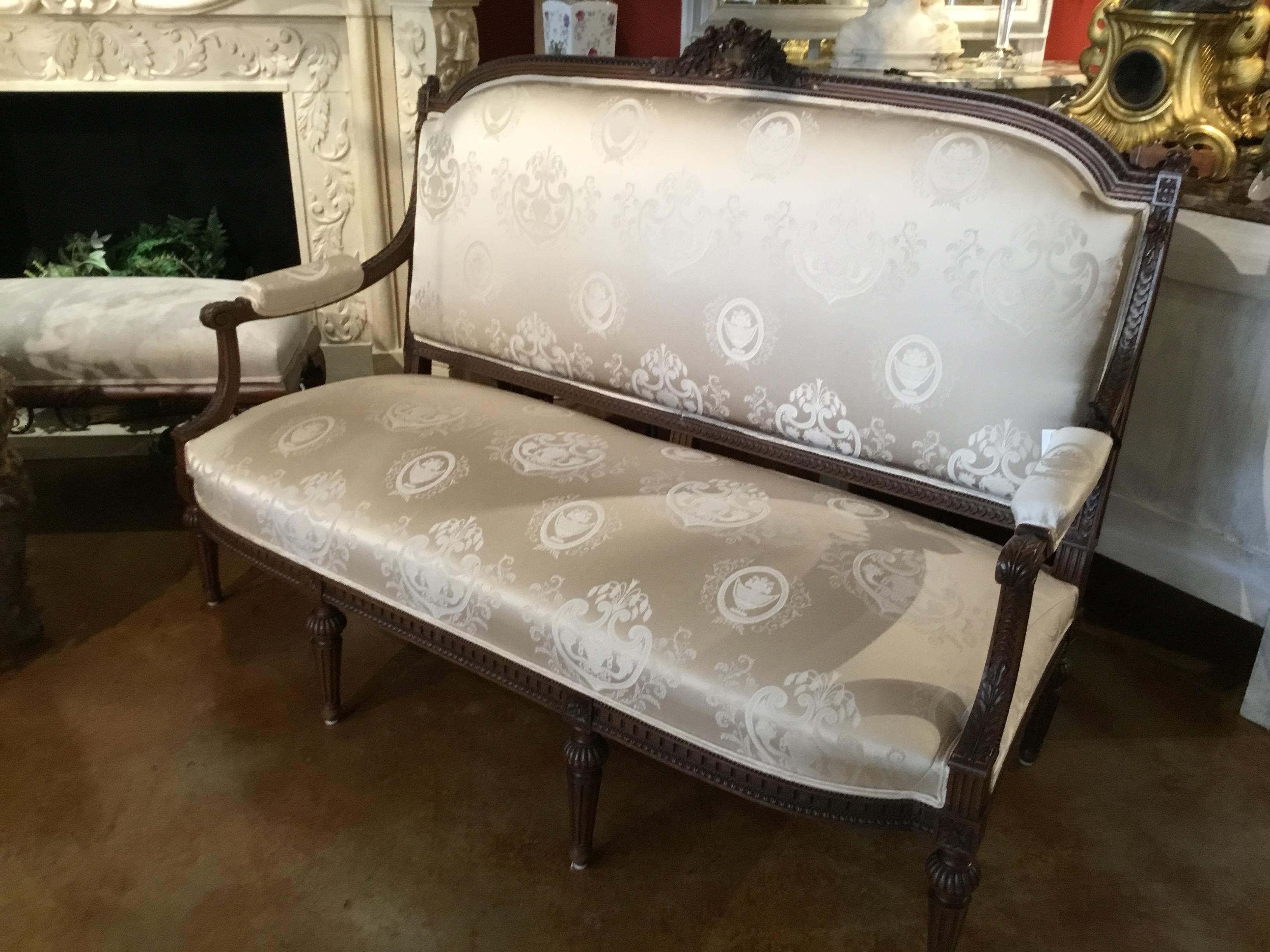 Beautifully carved frame in dark walnut finish with a carved wreath of roses
at the crest. Having a reeded carved leg and a shaped and delicately
curved arm. It is newly upholstered in a lovely white silk fabric in a French
motif.