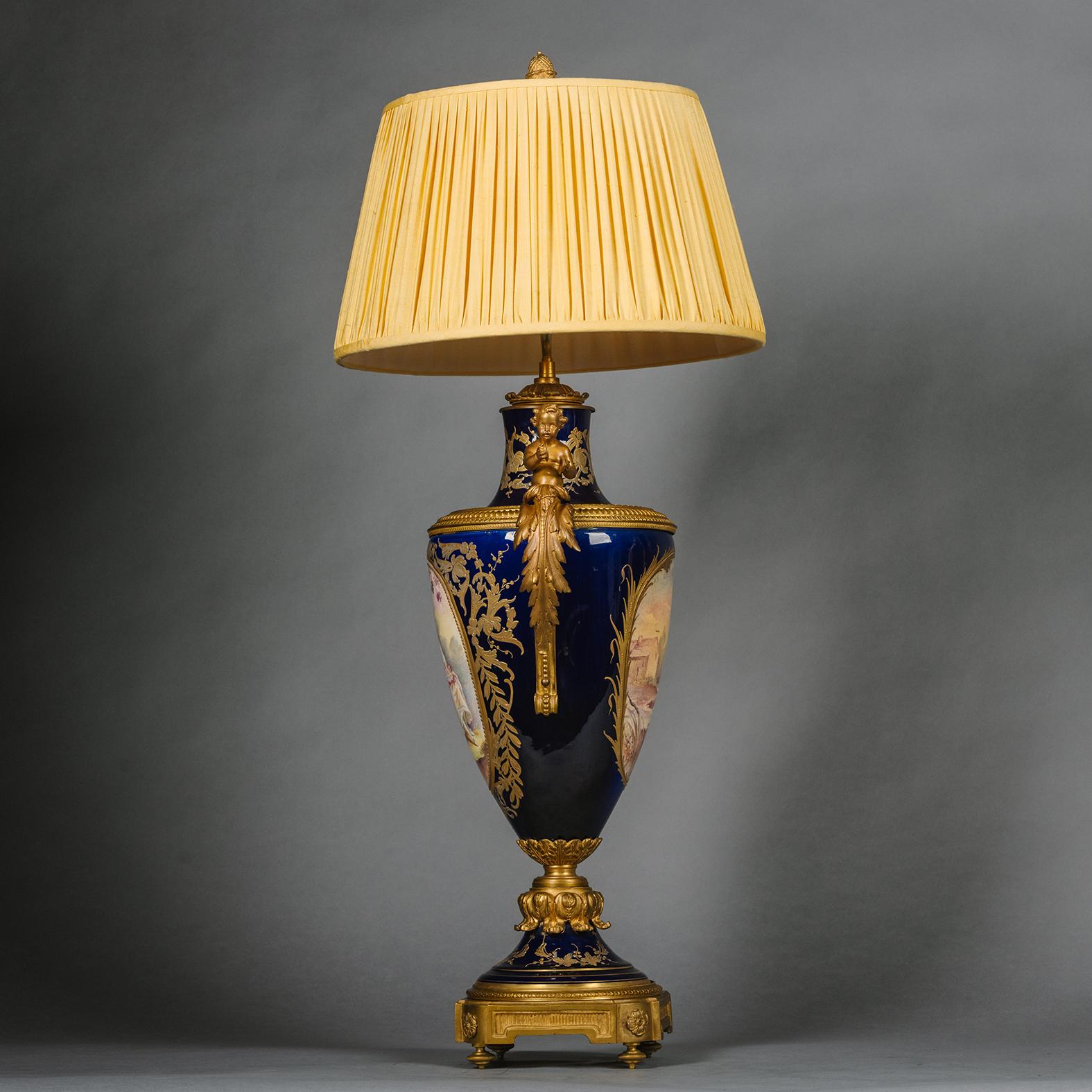 A Louis XVI Style Gilt-Bronze and Sèvres Style Cobalt-Blue Ground Porcelain Vase, Fitted as a Lamp.

Fronted by an oval portrait depicting a Rococo Style couple at the music lesson. The reverse of the vase with a lakeland vista. The handles modelled