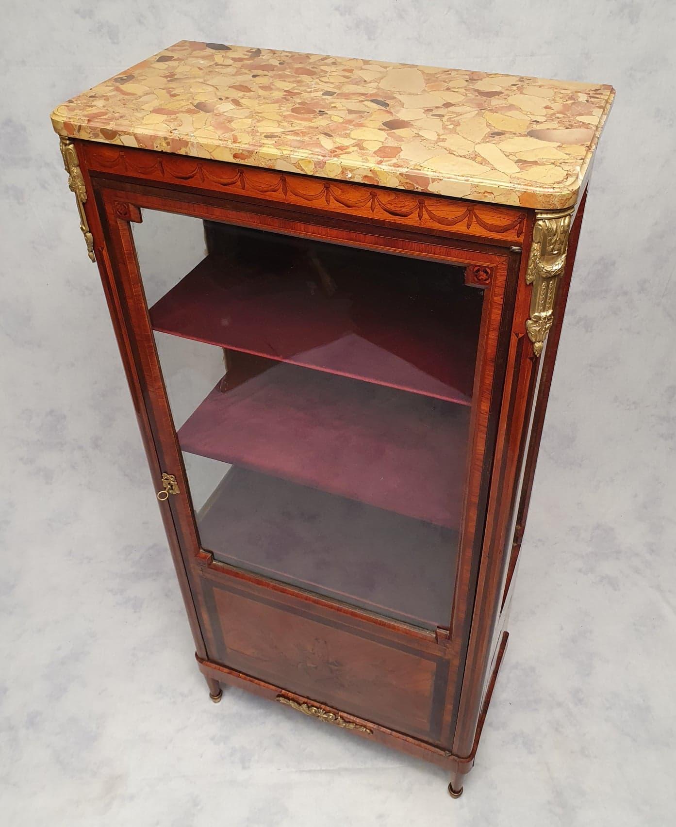 Louis XVI style showcase from the early 19th century. It presents a beautiful marquetry on the facade as on the ribs. The hunting trophy decorations of this marquetry are of good quality. In addition, a garland marquetry is on the top rail. Most of