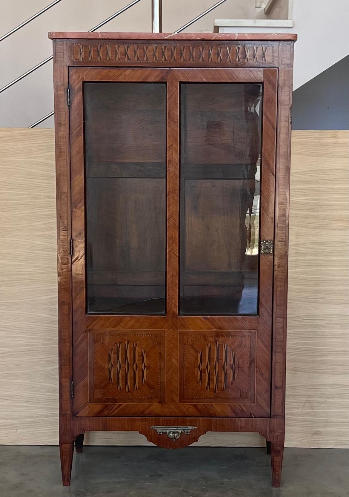 Vitrine de style Louis XVI du début du 19ème siècle. Il présente une belle marqueterie géométrique sur la façade comme sur les nervures. Les décorations de trophées de chasse de cette marqueterie sont de bonne qualité. En outre, une guirlande en