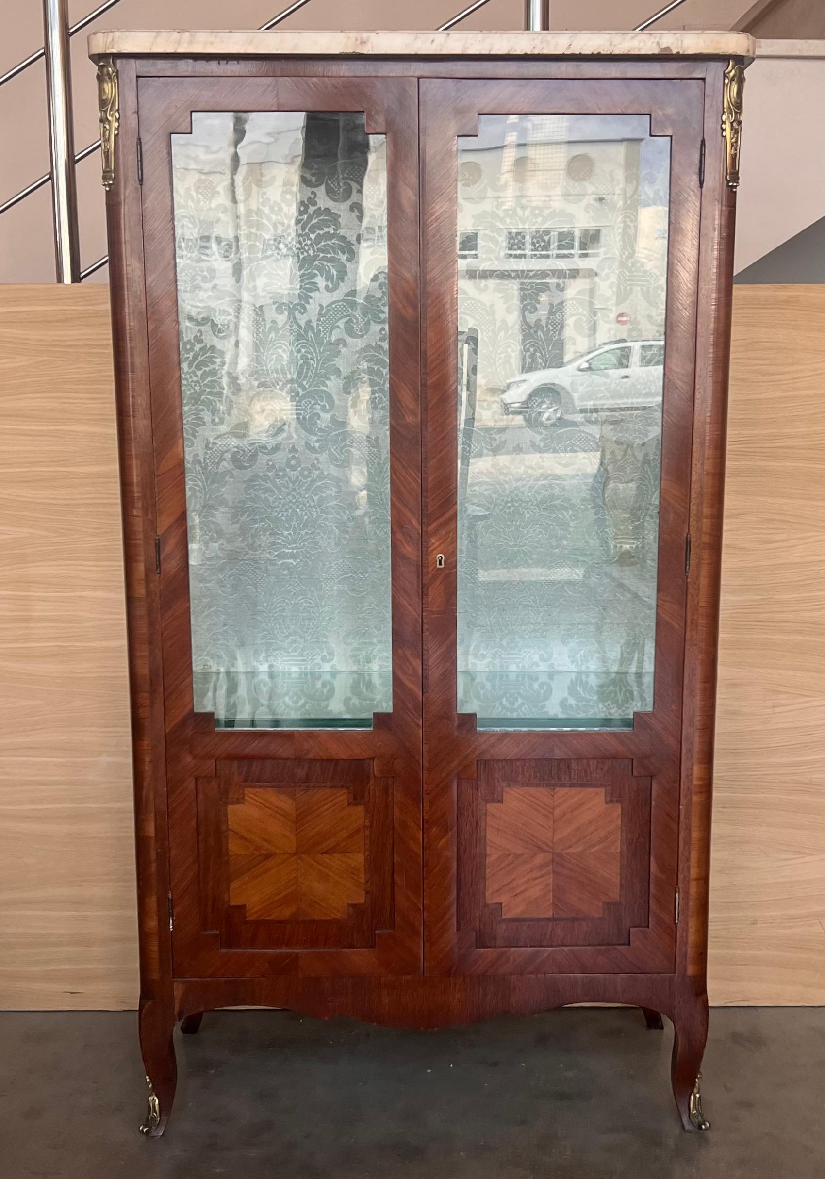 Louis XVI style showcase from the early 19th century. It presents a beautiful geometrical marquetry on the facade as on the ribs. The hunting trophy decorations of this marquetry are of good quality. In addition, a bronze garland  is on the bottom