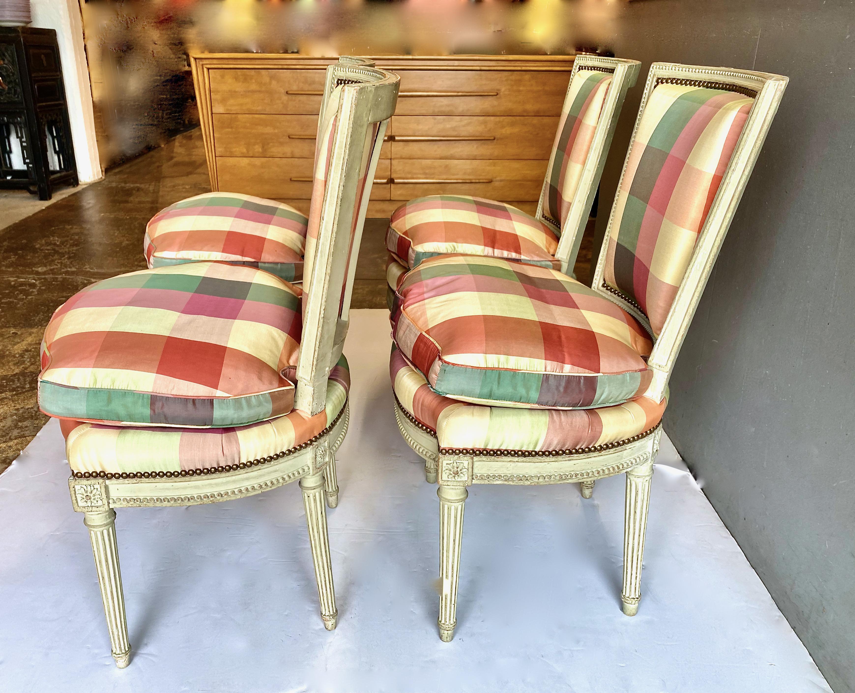 This is a stunning set of four Louis XVI-Style side chairs featuring hand carved fluted legs and beading surrounding the frame of the chairs. The chairs are painted in a traditional pale gray/green. The chairs retain a vintage plaid silk taffeta
