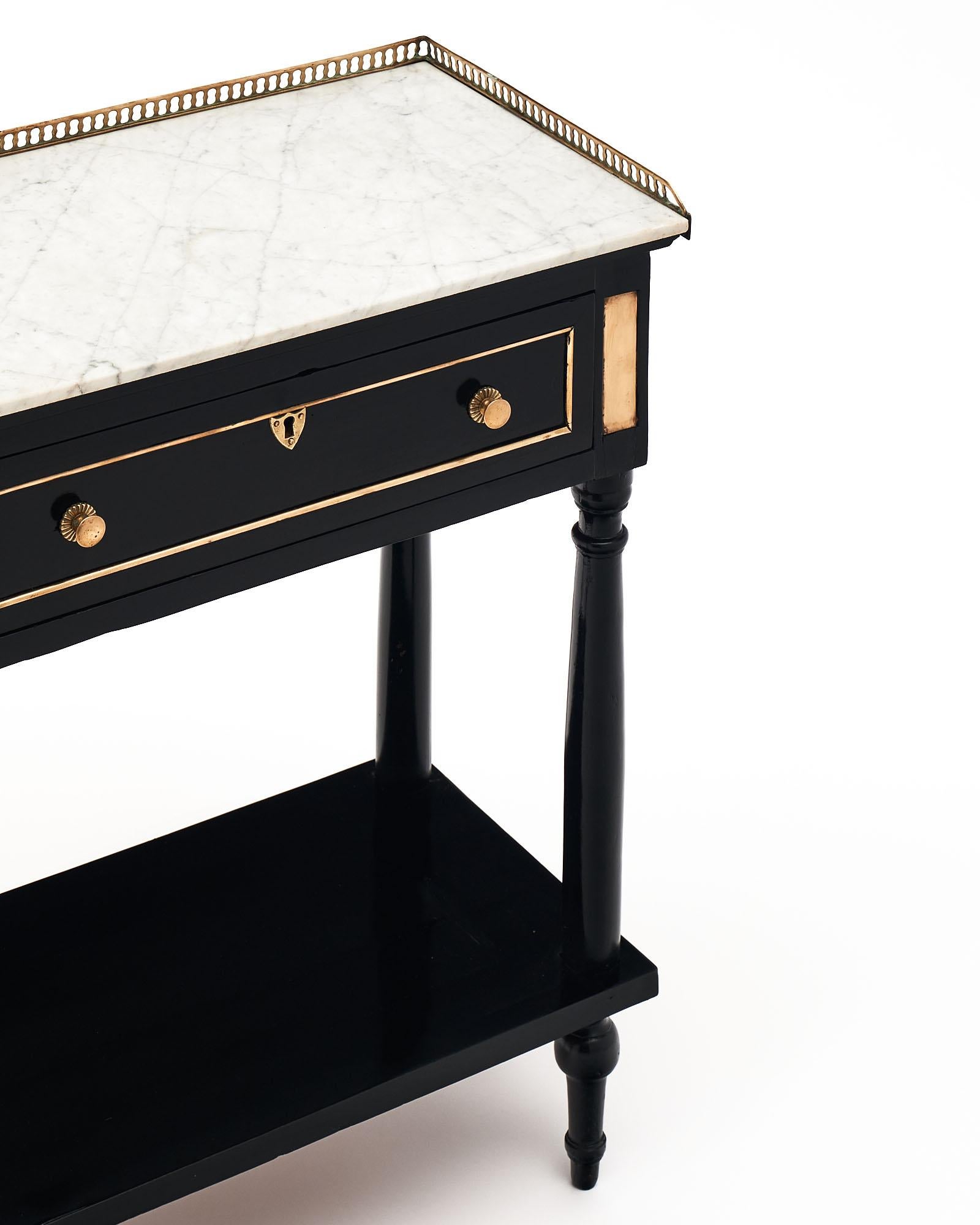 Side table in the Louis XVI style from France. This piece is finished in an ebonized French polish with a museum-quality luster. The Carrara marble top is surrounded by an open brass gallery. Brass trim and detailing can be found throughout. There