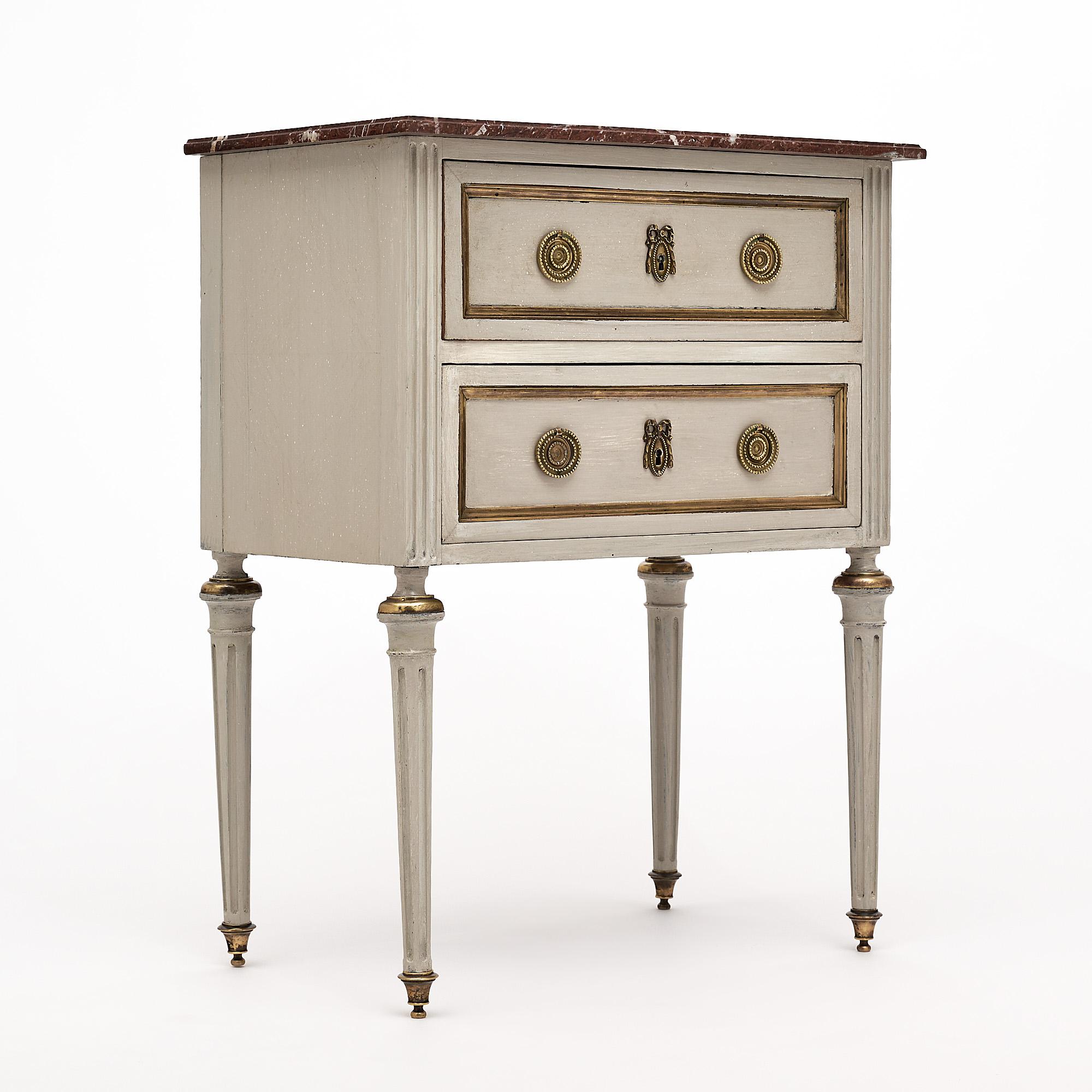 Side table, French, made of cherry wood with a “Trianon” gray paint finish. This piece has hand carved and fluted legs with finely cast hardware and trim throughout. There is a beautiful Rouge Royal marble top.