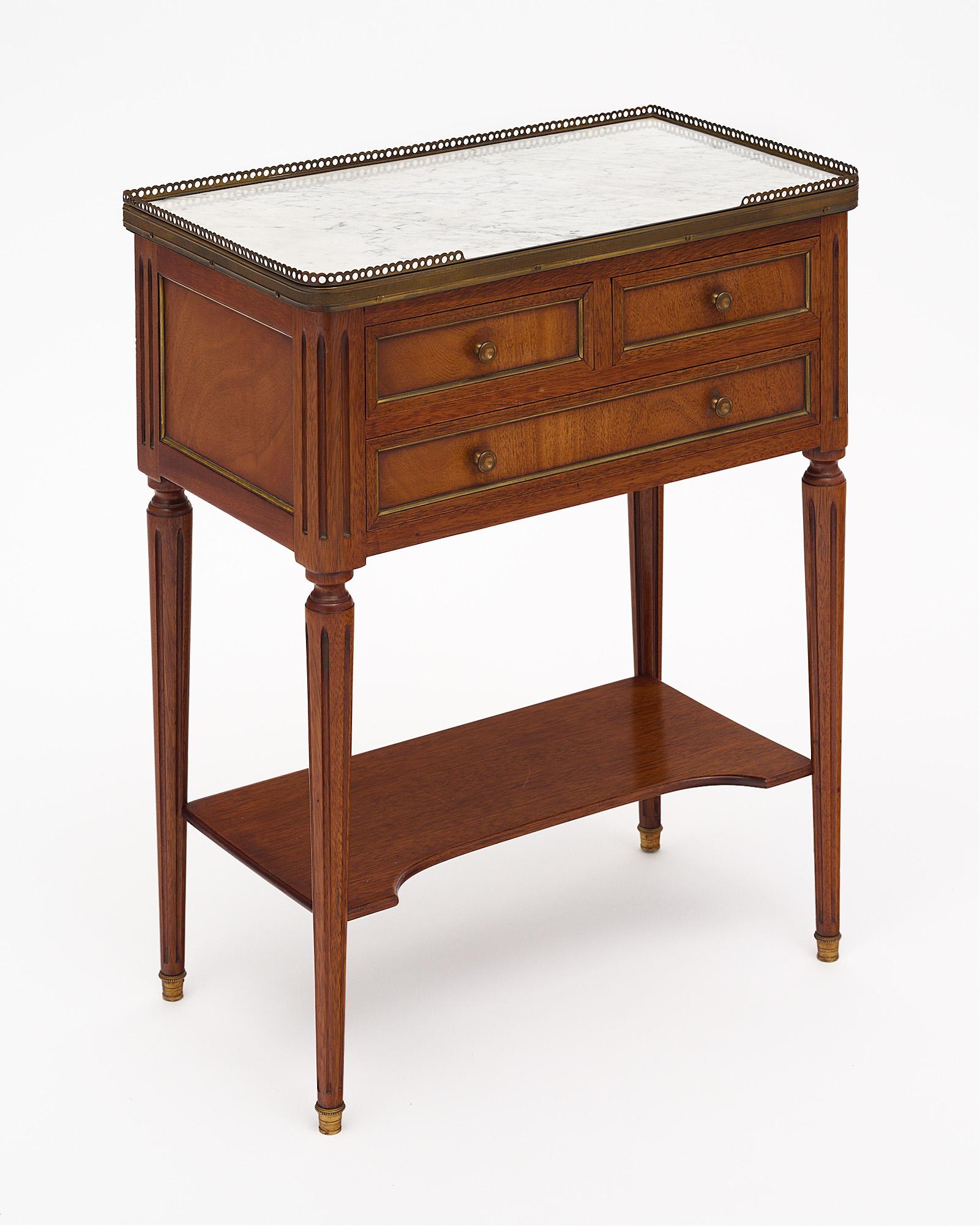 Side table in the Louis XVI style from France featuring a Carrara marble top and brass trim throughout. This piece has three dovetailed drawers and tapered; fluted legs. It has been finished with a lustrous French polish for a museum-quality shine.