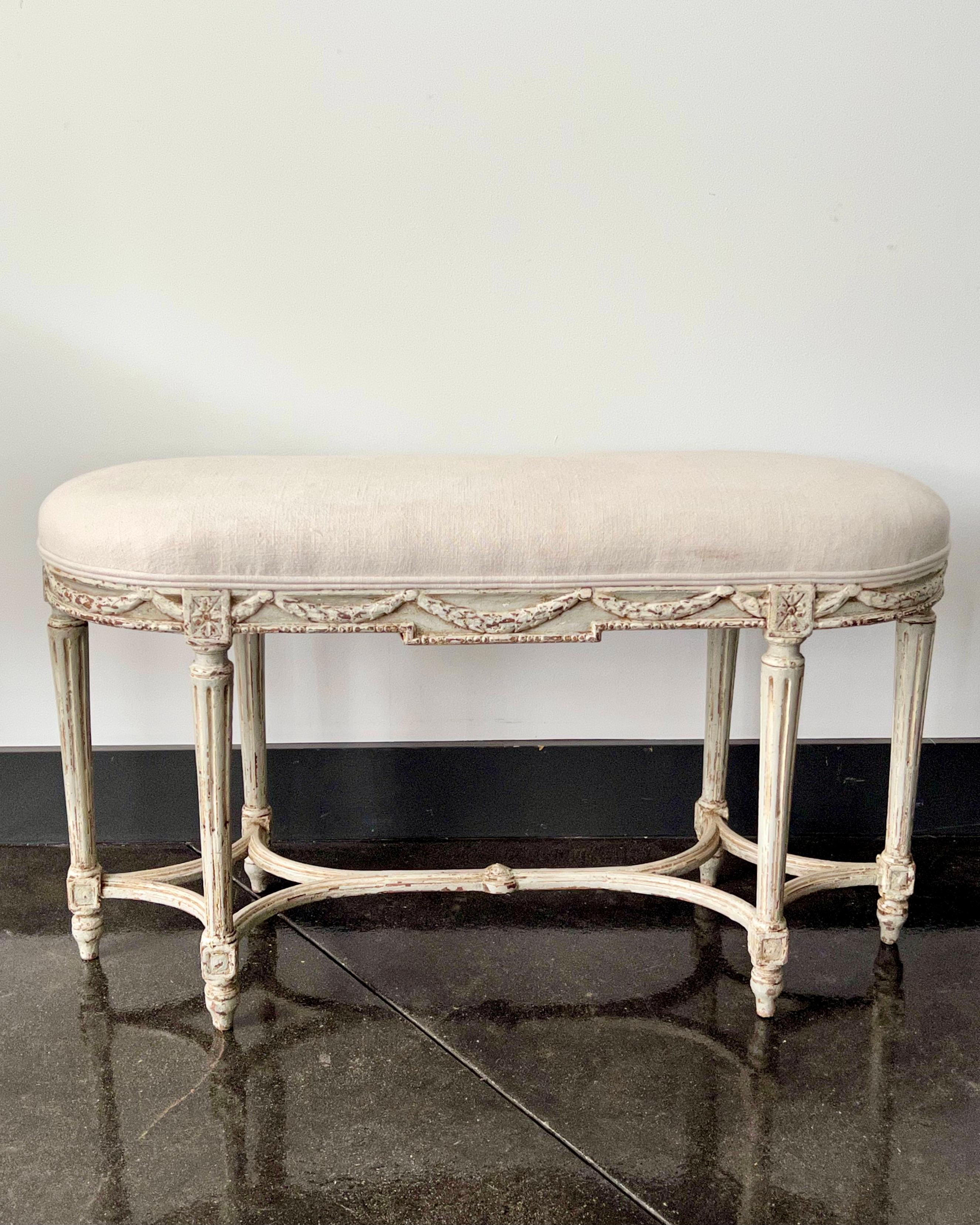 A small bench in Louis XVI style with scalloped frieze carved in floret motifs, raised on tapered legs and joined with double x-curved stretchers. Upholstered in linen. 
 