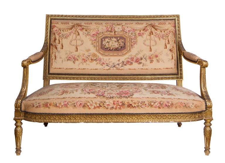 A 19th century French Louis XVI style five piece salon suite, consisting of a sofa and four matching armchairs. All five pieces have intricately carved giltwood furniture frames and are upholstered with French-made Aubusson tapestry fabric. Overall
