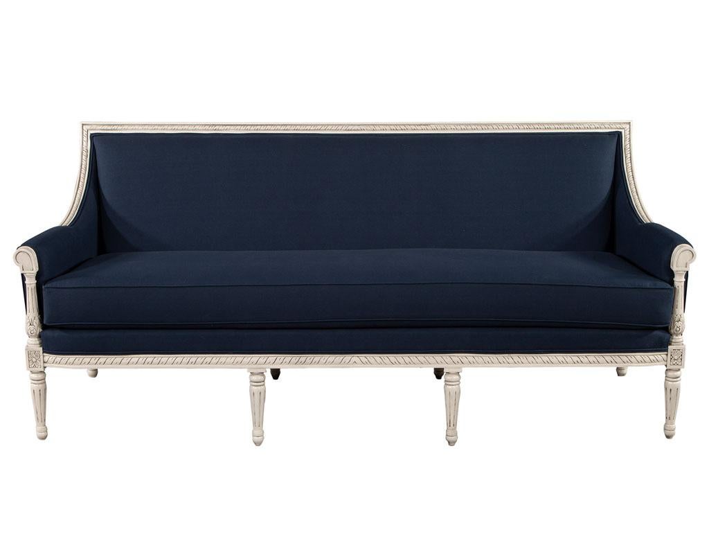 Louis XVI style sofa in Indigo Navy blue fabric. Beautiful Louis XVI inspired frame with floral carvings and details. Finished in a distressed off-white cream with dark glaze to accentuate the detailing. Completed with thick cushion upholstery work