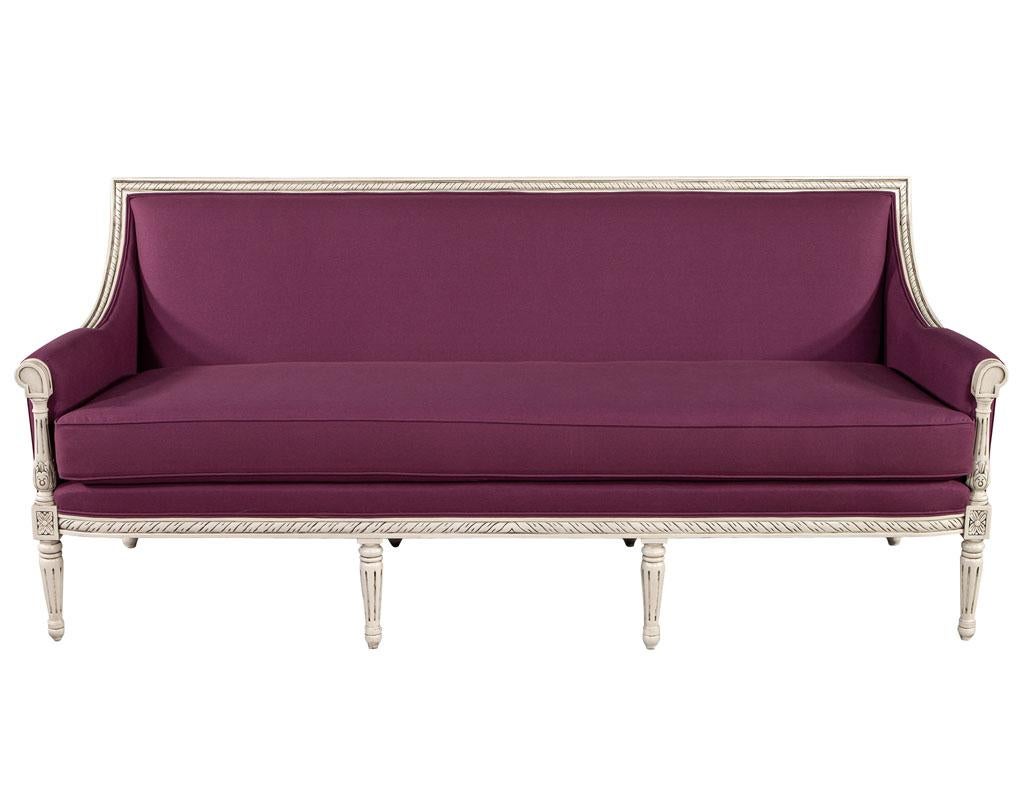 Louis XVI style sofa in Plum Burgundy fabric. Beautiful Louis XVI inspired frame with floral carvings and details. Finished in a distressed off-white cream with dark glaze to accentuate the detailing. Completed with thick cushion upholstery work in