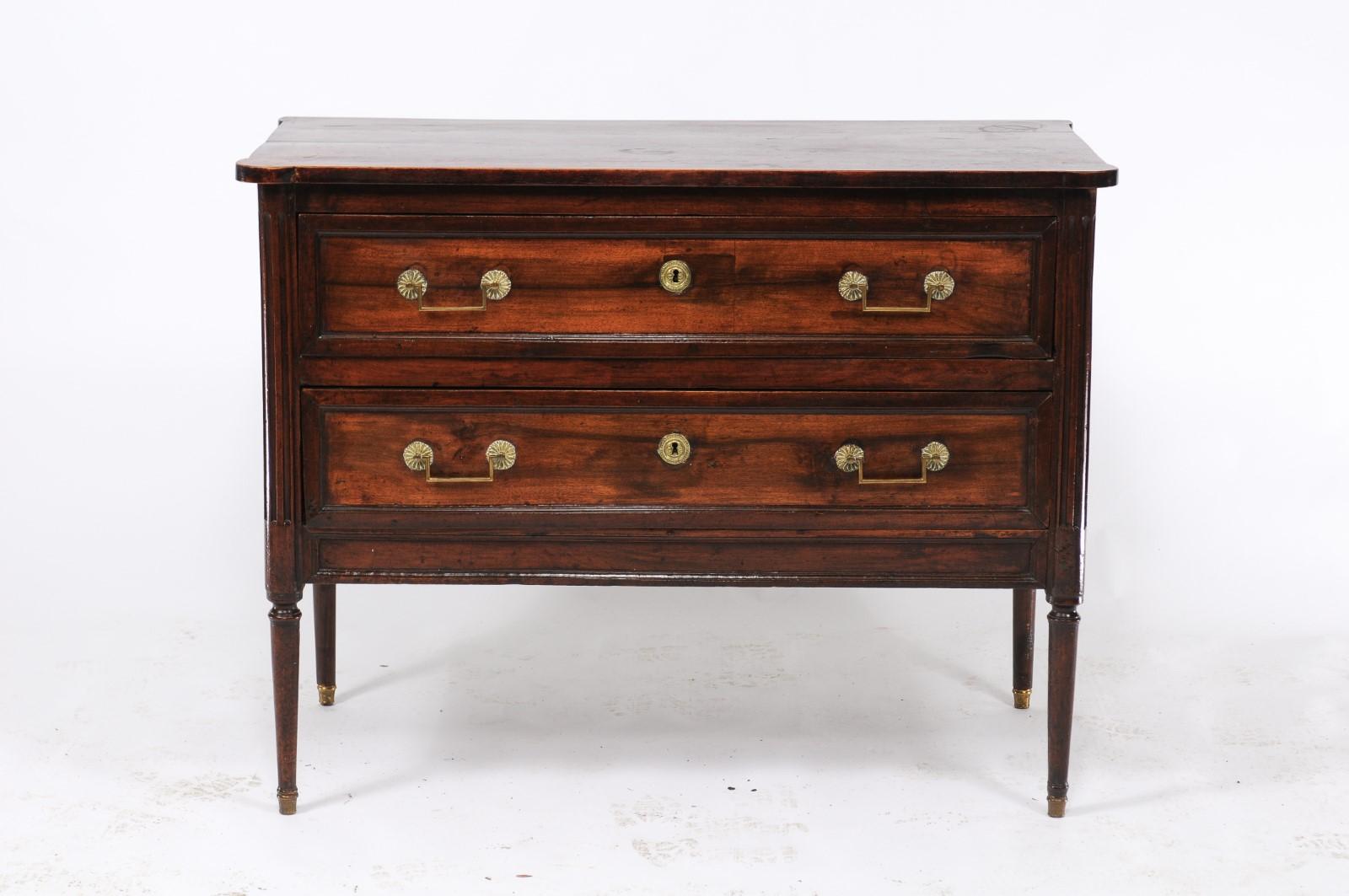 A southwestern French Louis XVI style walnut commode from the second half of the 19th century, with two dovetailed drawers, linear brass hardware, cylindrical tapering legs and fluted side posts. Its elegant and clean lines, classic hardware, two