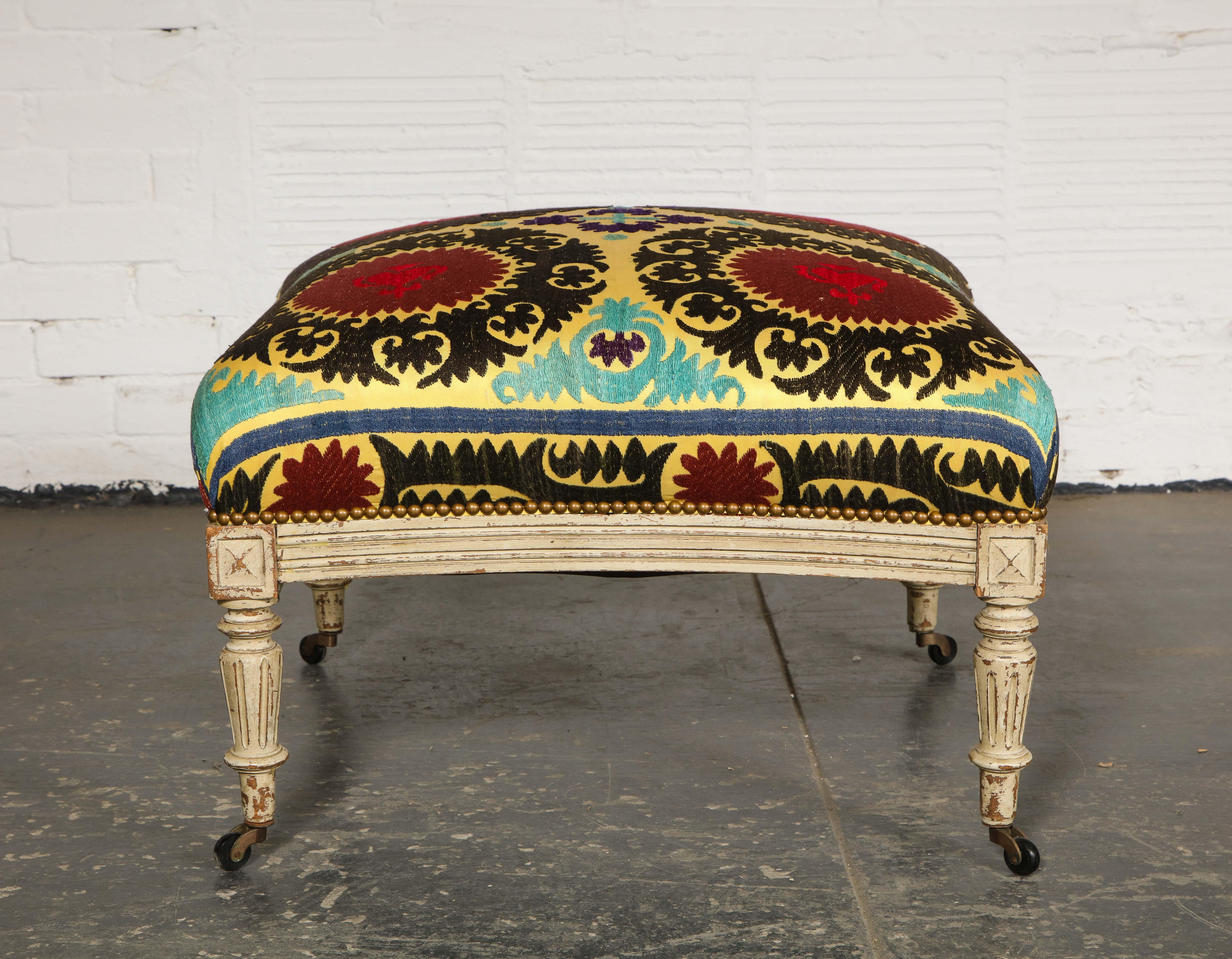 The square seat with incurved side upholstered in a yellow-ground Suzani textile; raised on tapering legs on casters.