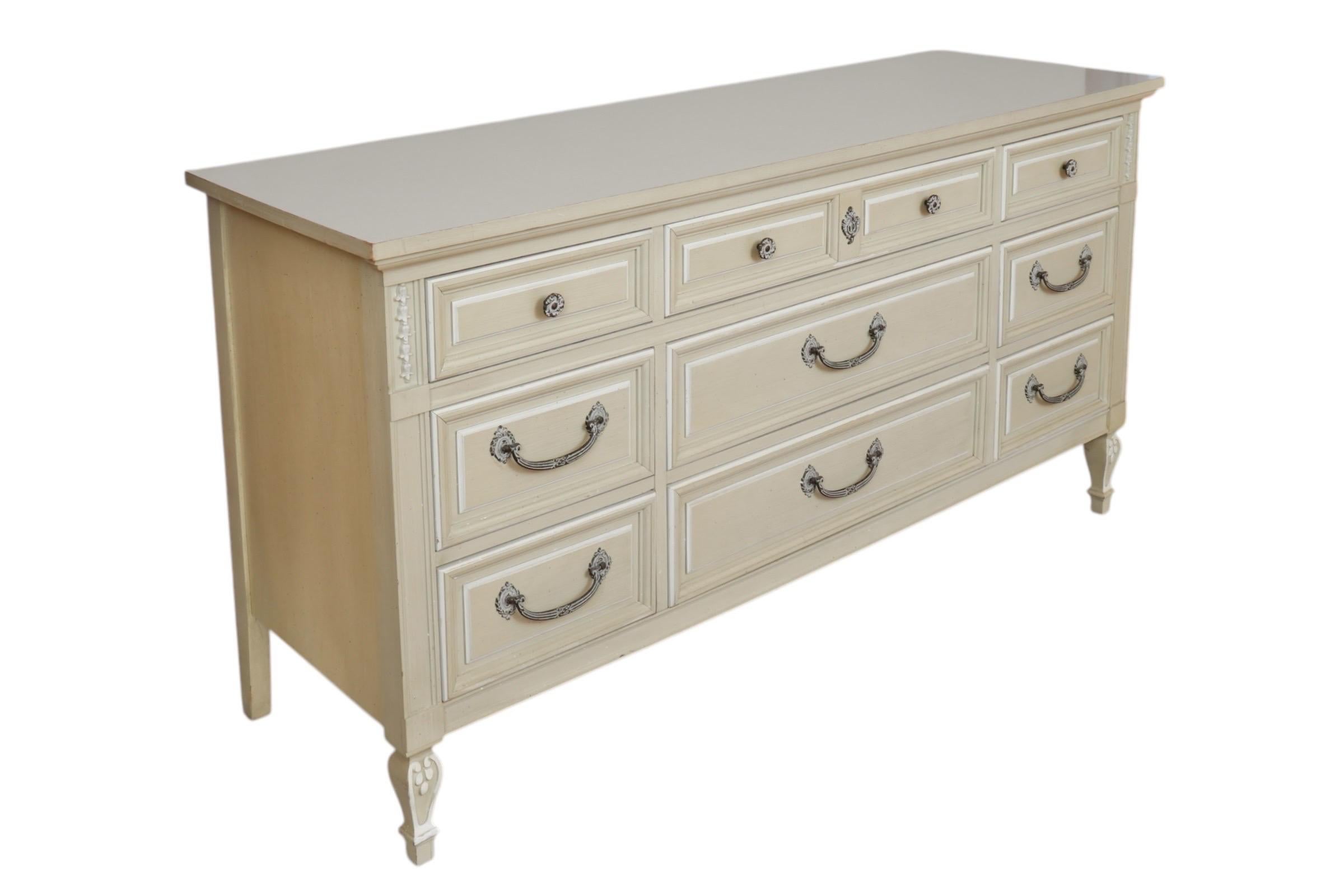 Un comò triplo in stile Luigi XVI realizzato da Dixie Furniture nel 1970 circa. I tre cassetti superiori sono pannellati per dare l'impressione di essere quattro e si aprono con maniglie a rosetta con pomello. Anche i cassetti inferiori sono