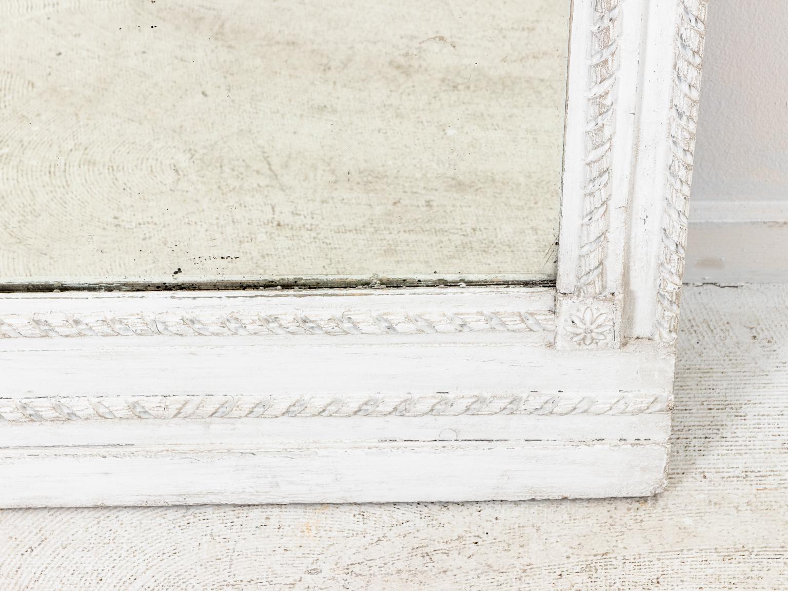 Painted white and grey mirror with Roman floral swag detail in upper panel and ribbon banderol trim, circa 19th century. Made in France. Please note of wear consistent with age such as repainting, and a modern replacement of the top mirror. The