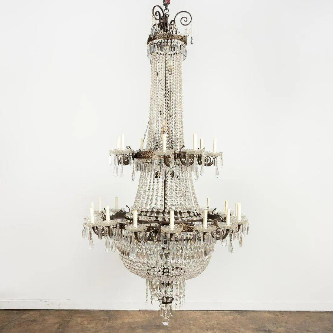 Large scale two-tier basket chandelier in the Louis XVI style, having a bronze-tone frame hung with faceted crystal swags and pendants, the coronas decorated with scrolled anthemion, the lower two issuing a total of twenty-eight scrolled arms, and