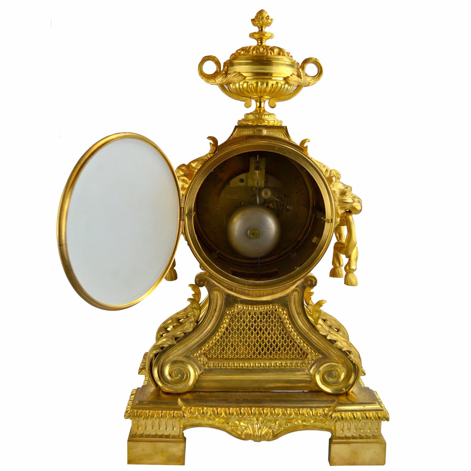 A gilt and chiseled bronze Louis XVI style mantle clock after a popular model of the late 18thC in France. The clock is topped with a large gilded lidded urn and has lion's muzzles holding loops on either side of the clock dial and plinth. The dial