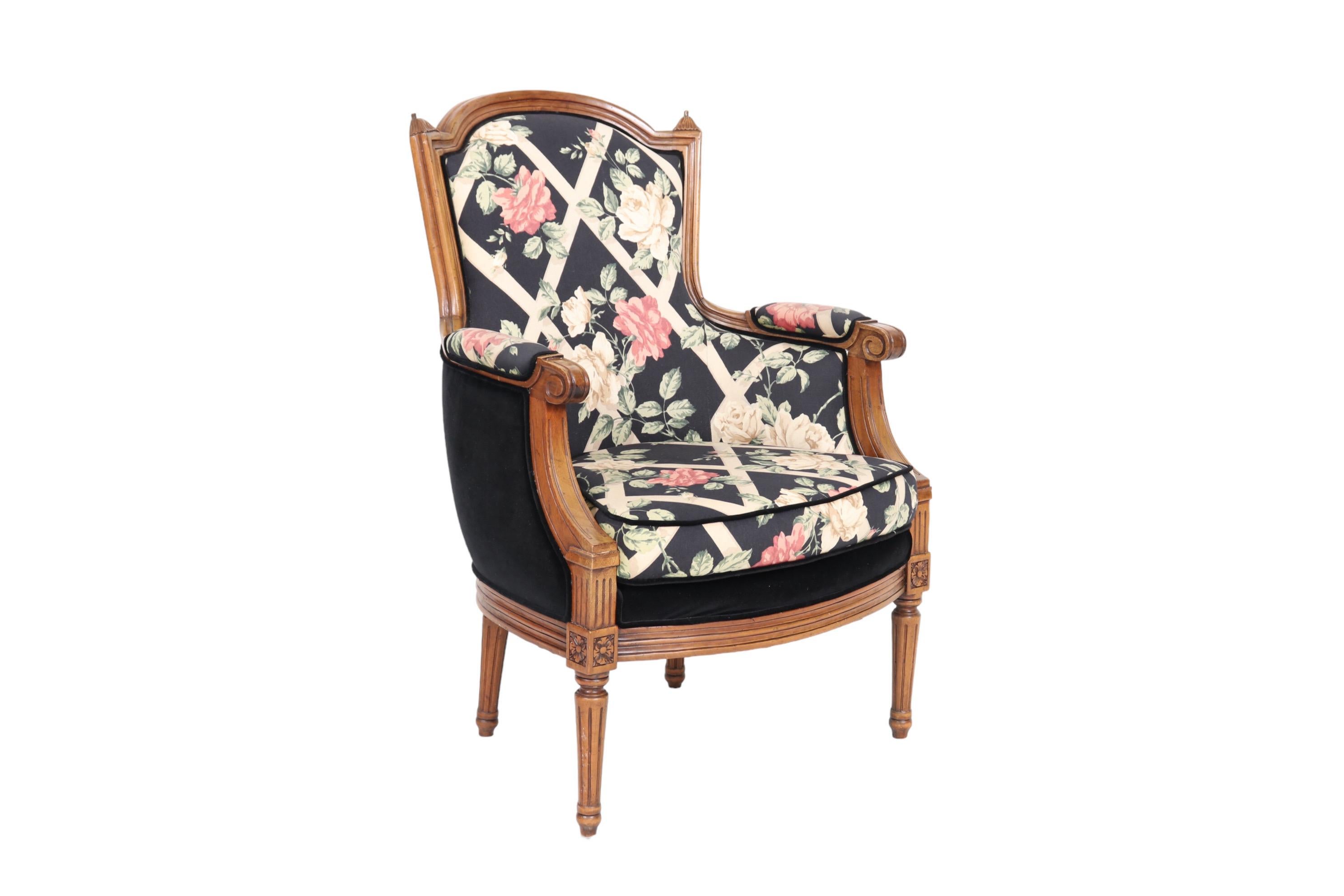 A Louis XVI style bergère armchair made of walnut. The frame is beveled throughout with foliate finials at each side of the crest rail. Cushioned arms terminate in scrolled hand holds and rosettes in squares top fluted round tapered legs.